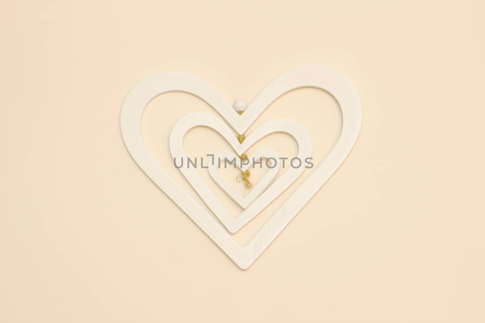 A three layer white heart made of wood hanging on a cream wall centered in the photo