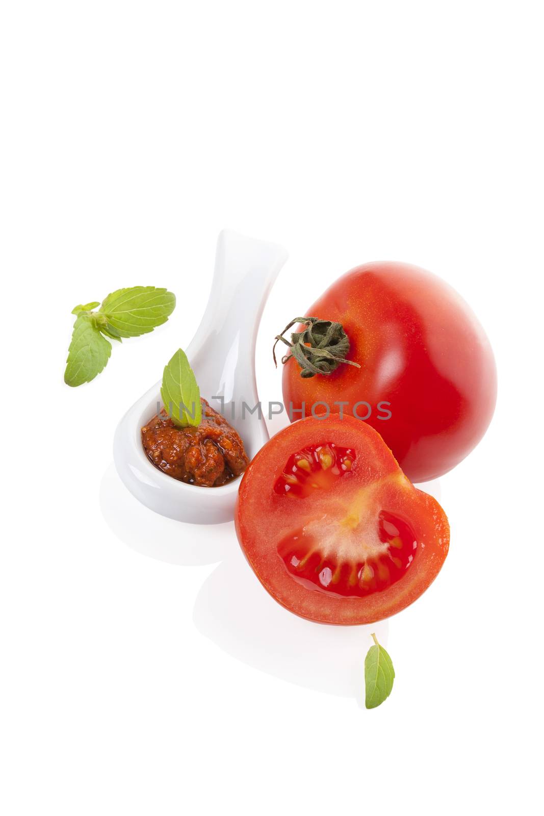 Fresh tomatoes and red pesto on spoon with fresh basil leaf isolated on white background. Culinary eating, minimal contemporary styles.