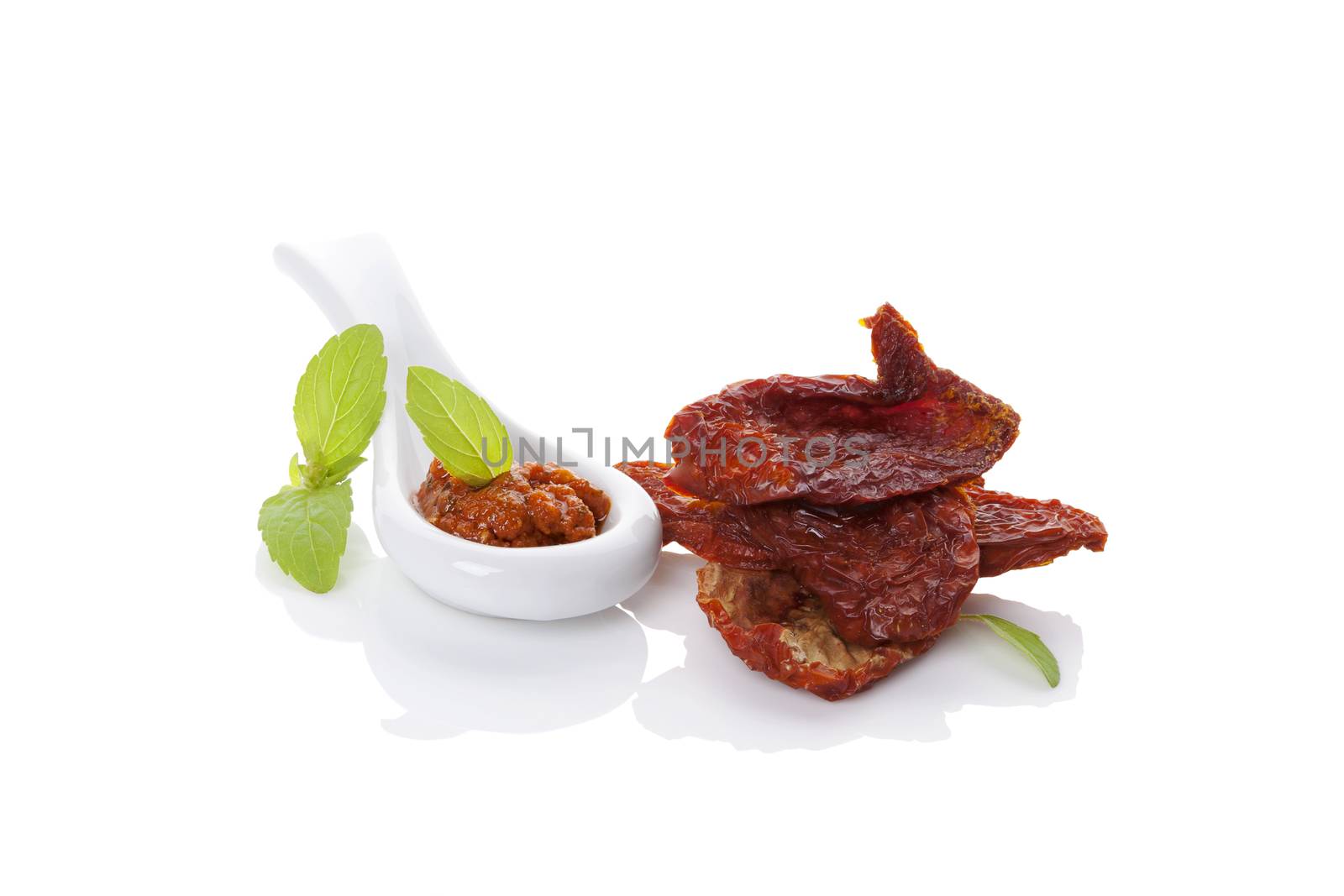 Red pesto and dry tomatoes on spoon with fresh basil leaf isolated on white background. Culinary italian eating, minimal contemporary styles.