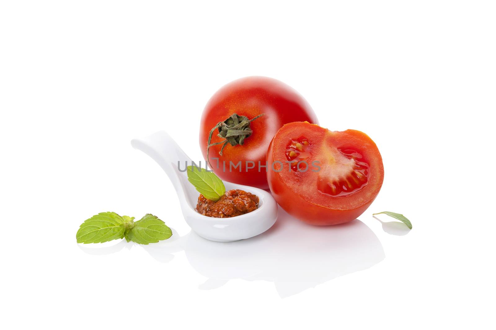 Fresh tomatoes and red pesto on spoon with fresh basil leaf isolated on white background. Culinary eating, minimal contemporary styles. 