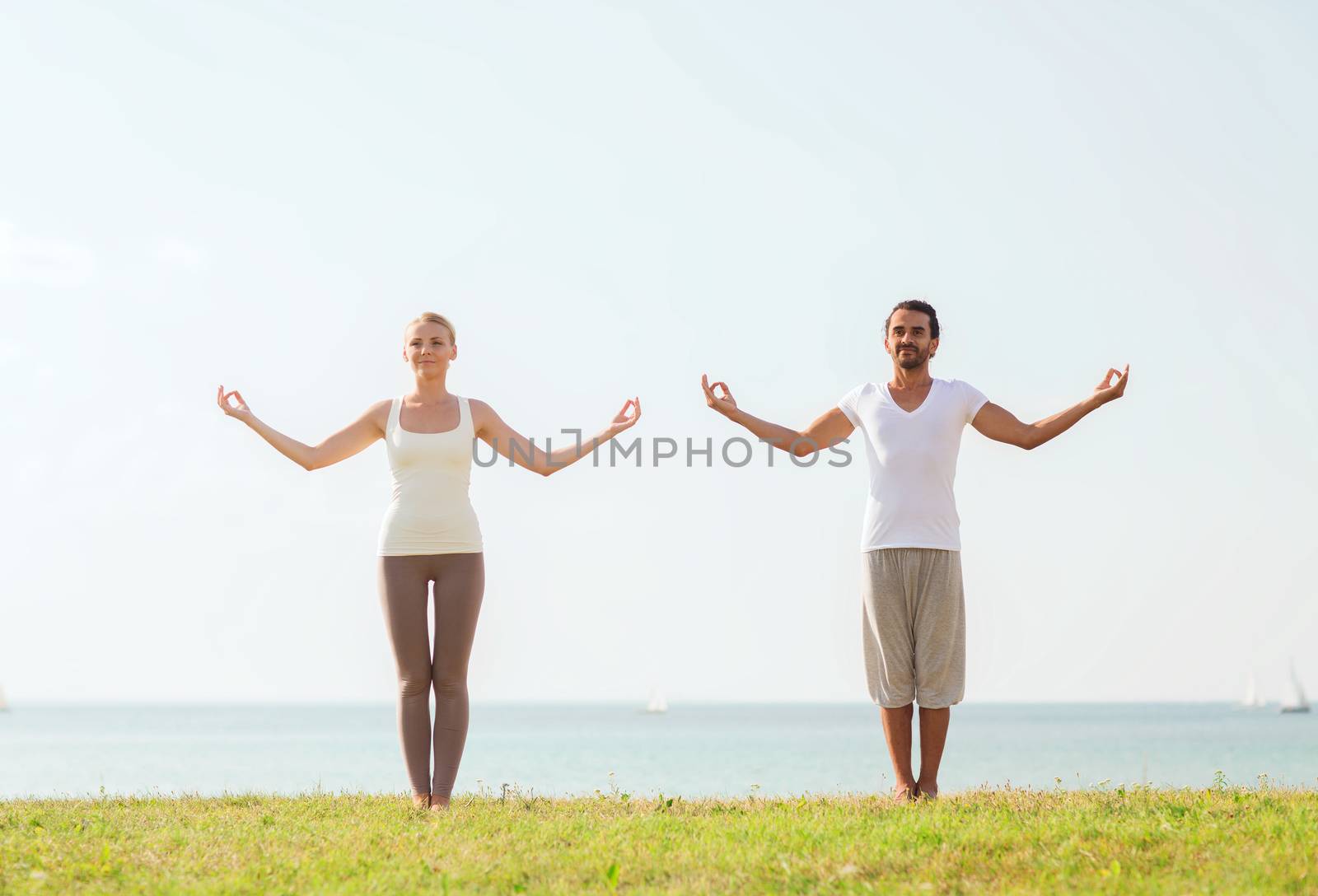 smiling couple making yoga exercises outdoors by dolgachov