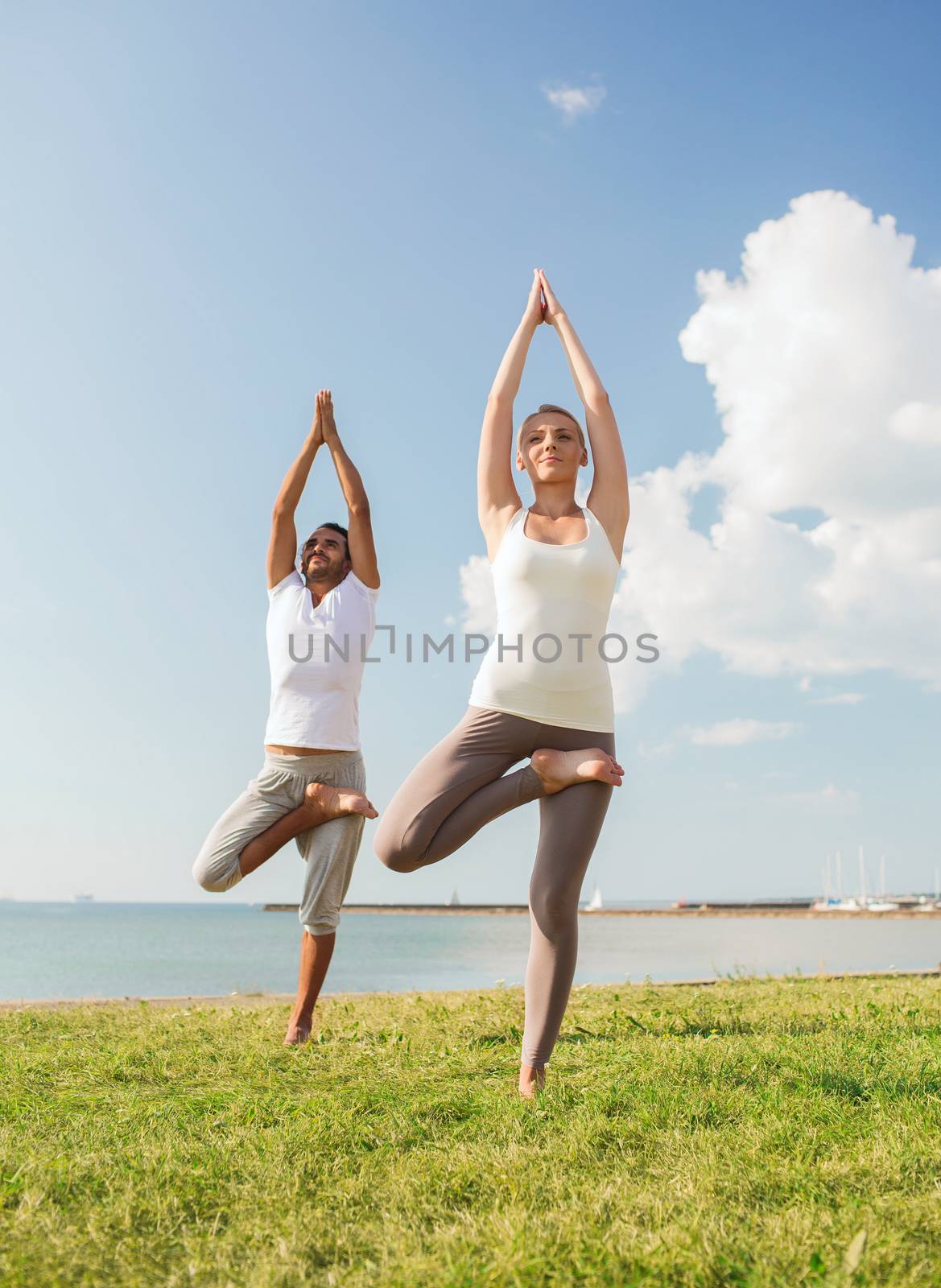 fitness, sport, friendship and lifestyle concept - smiling couple making yoga exercises outdoors