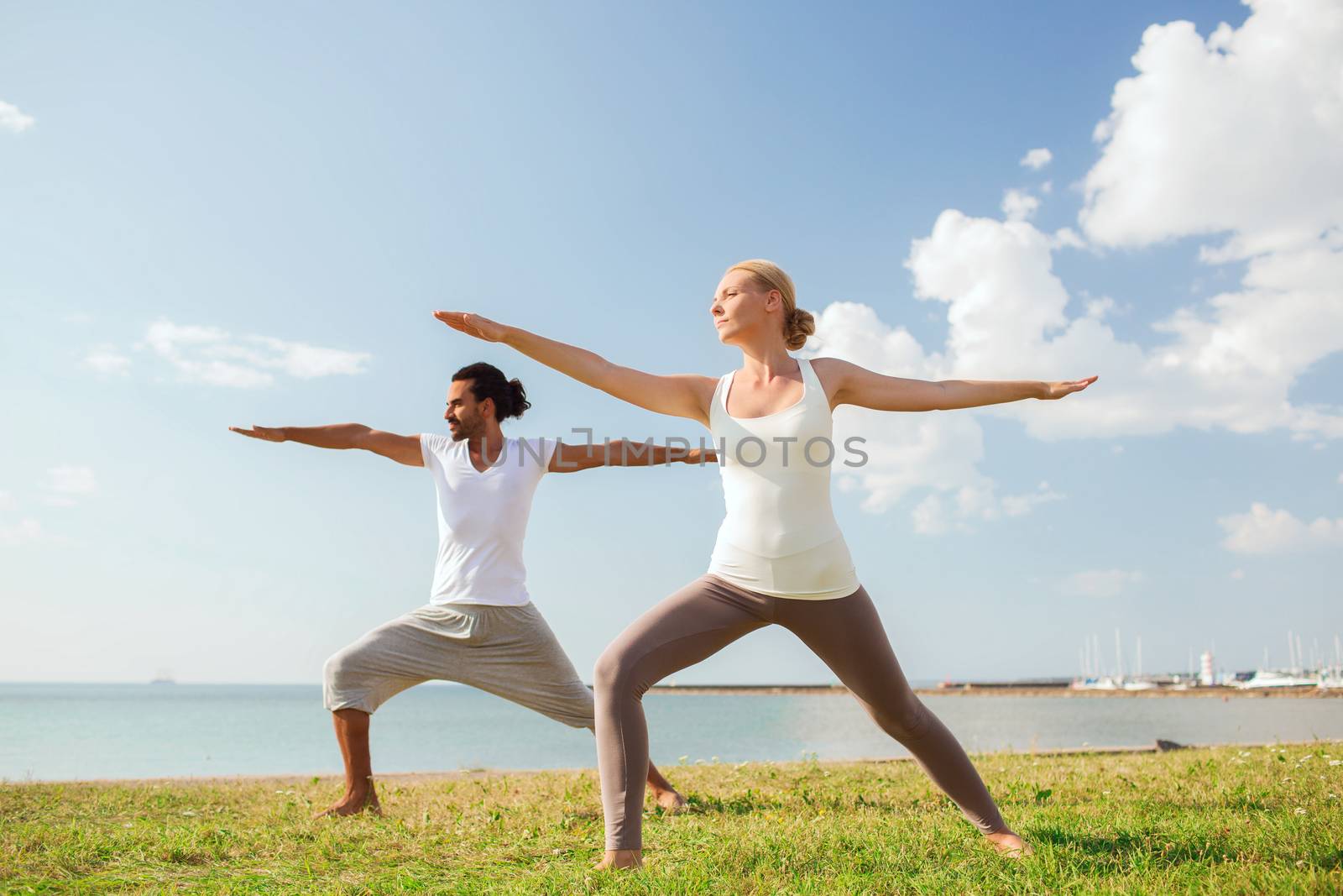 smiling couple making yoga exercises outdoors by dolgachov