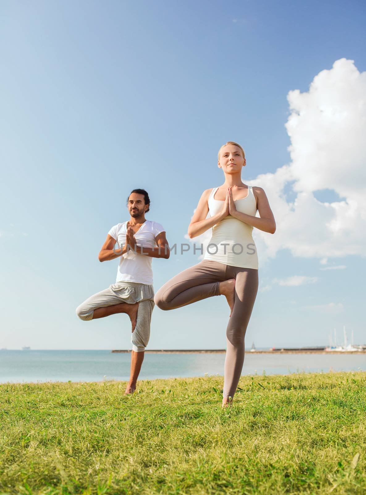 smiling couple making yoga exercises outdoors by dolgachov