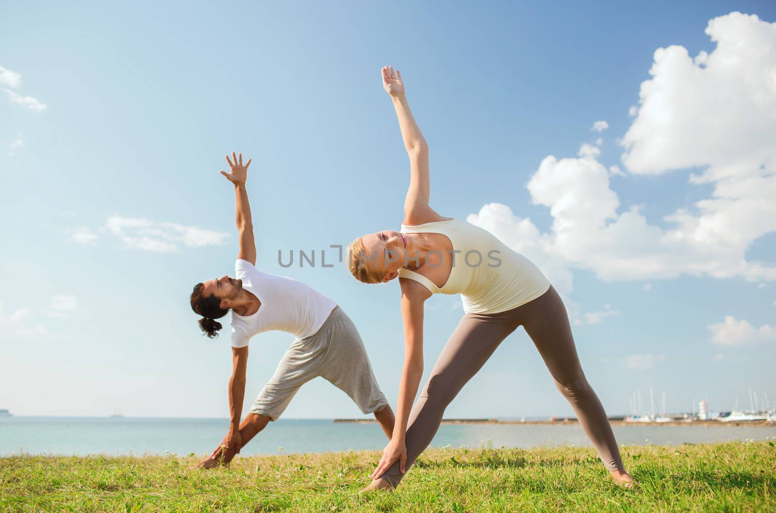 smiling couple making yoga exercises outdoors by dolgachov