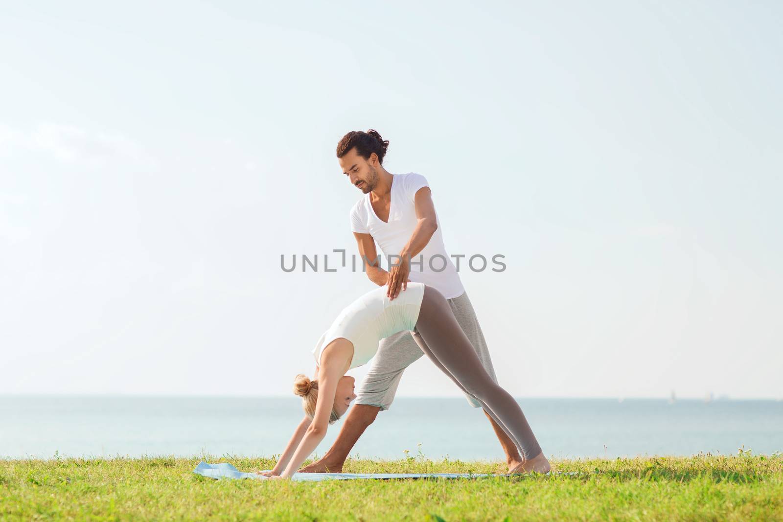 fitness, sport, friendship and lifestyle concept - smiling couple making yoga exercises on mat outdoors