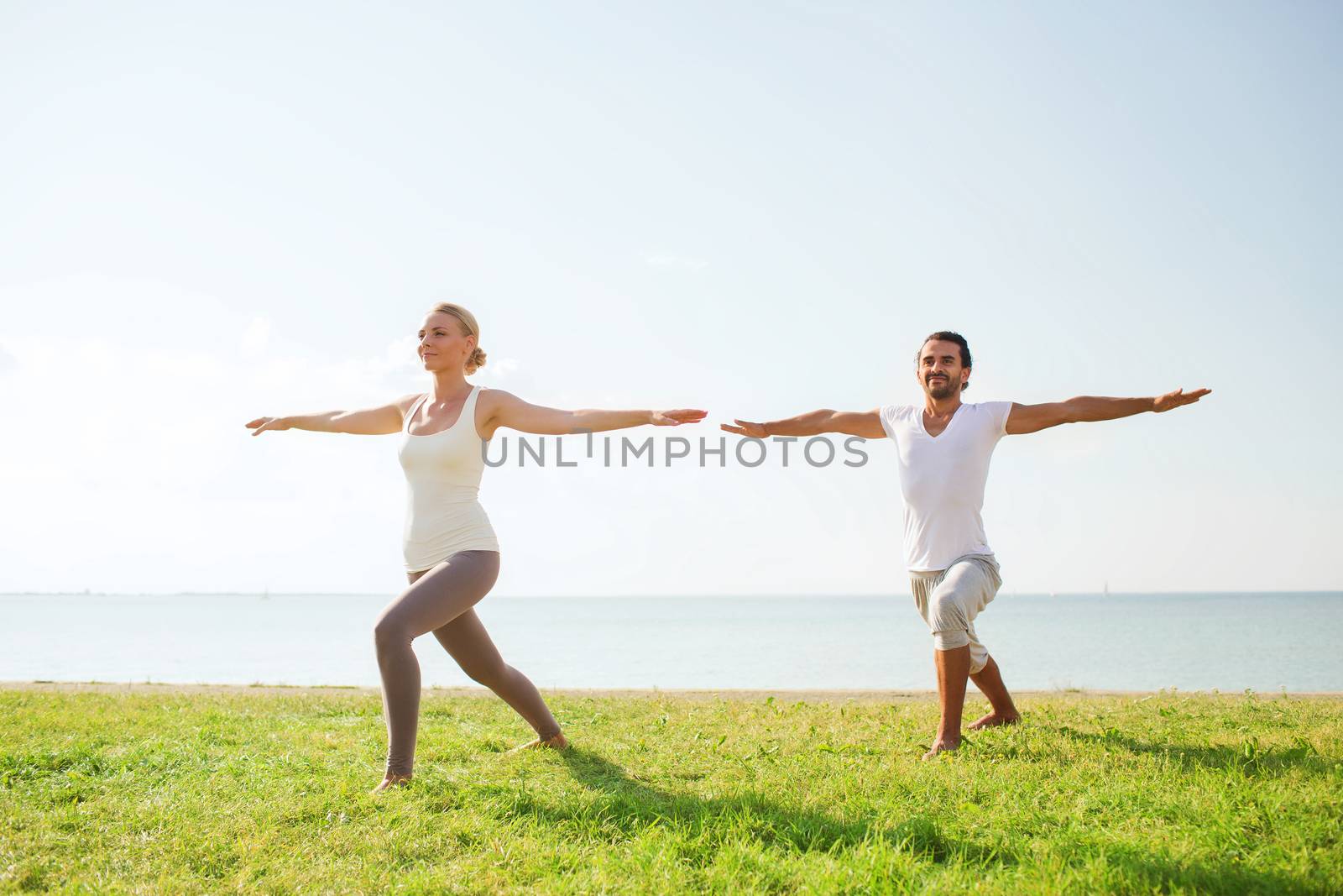 fitness, sport, friendship and lifestyle concept - smiling couple making yoga exercises outdoors