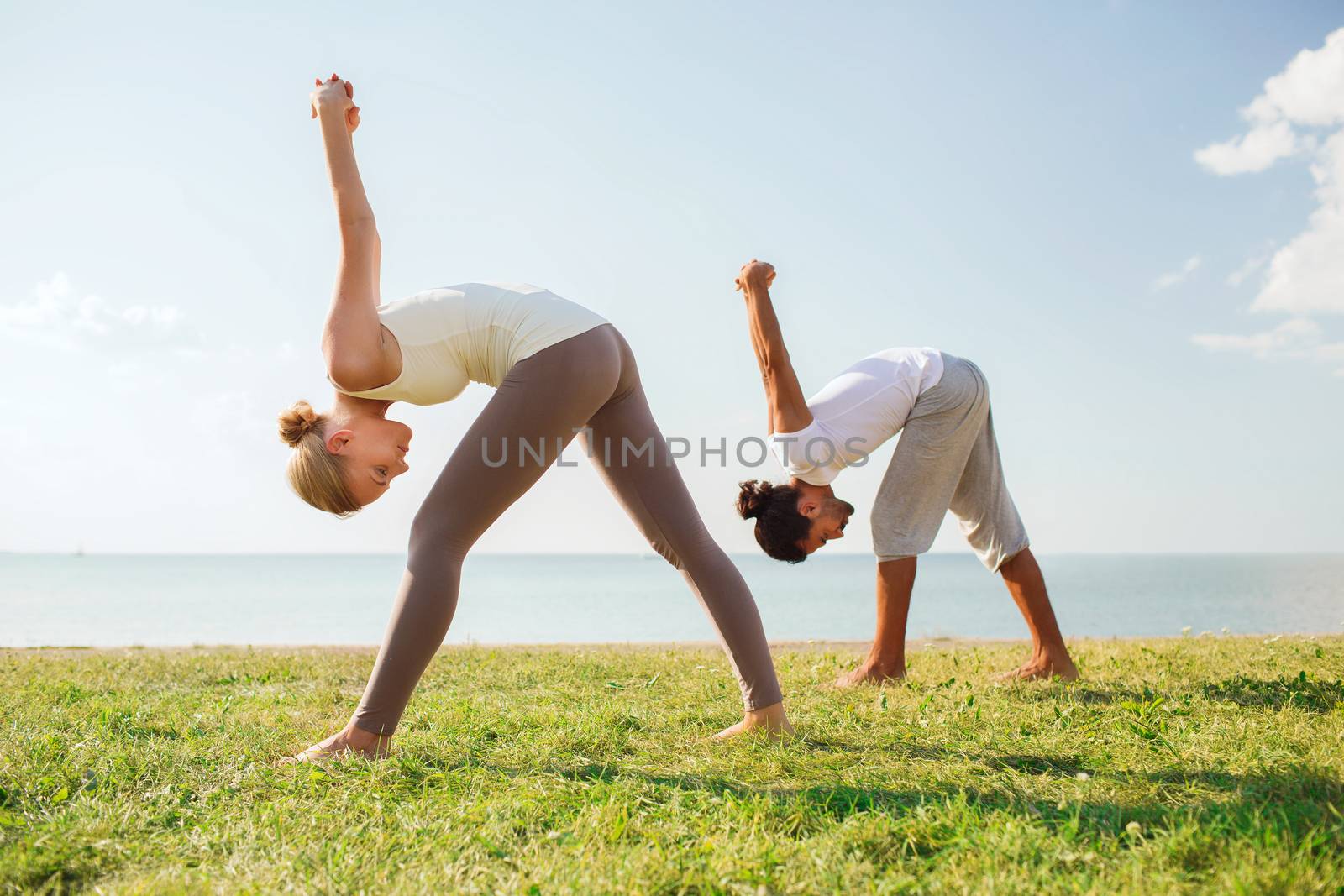 smiling couple making yoga exercises outdoors by dolgachov