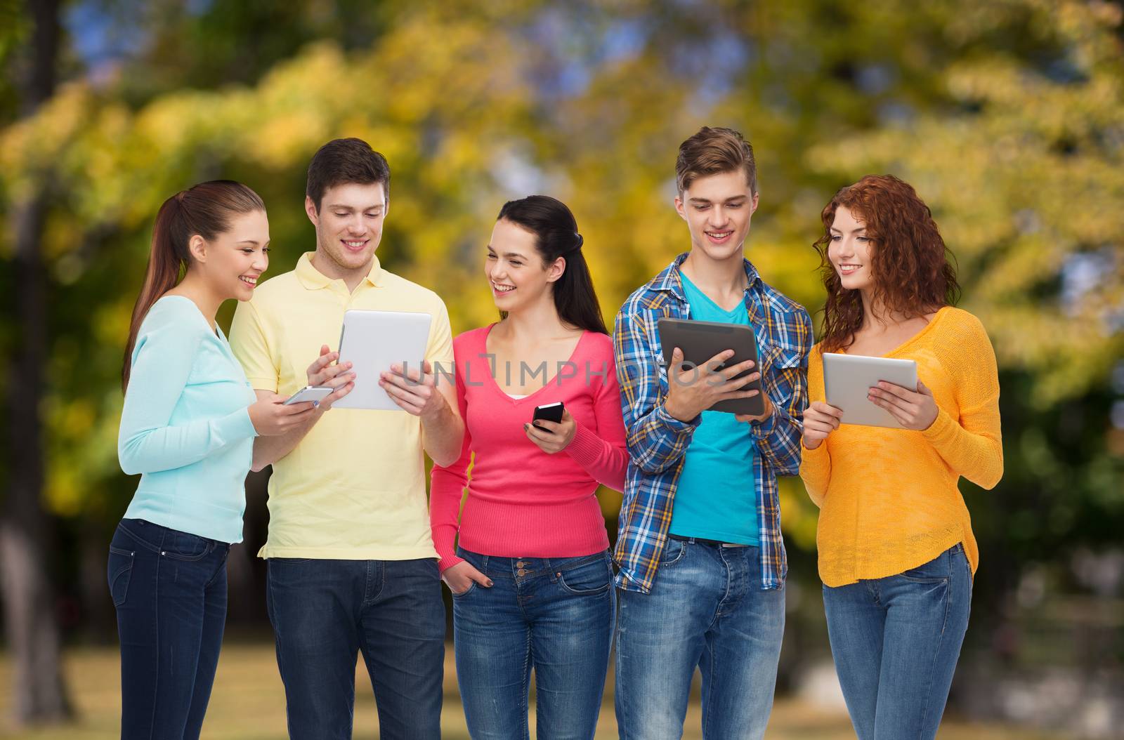 friendship, technology and people concept - group of smiling teenagers with smartphones and tablet pc computers over park background
