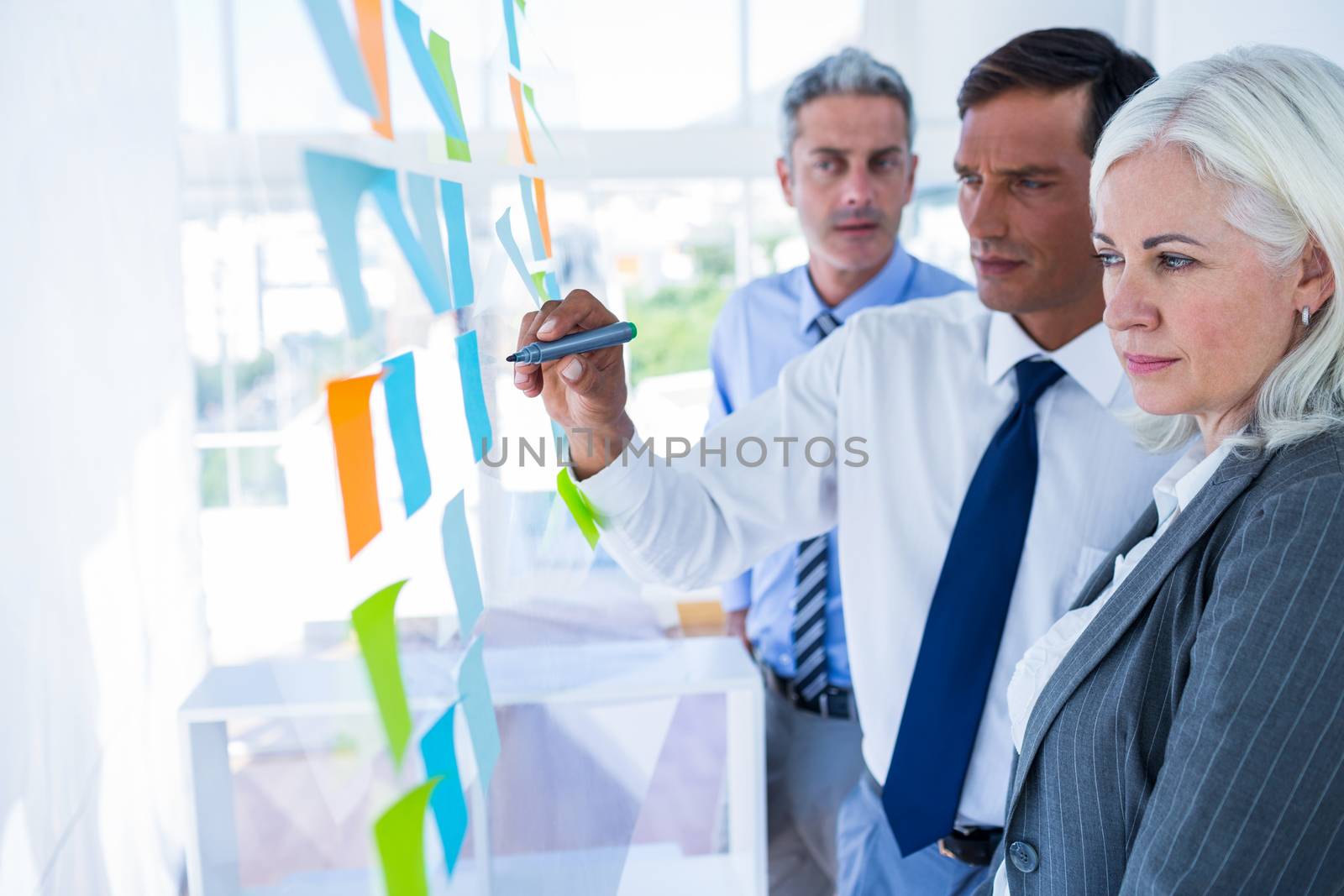 Businessman writing on post it with his colleagues  by Wavebreakmedia