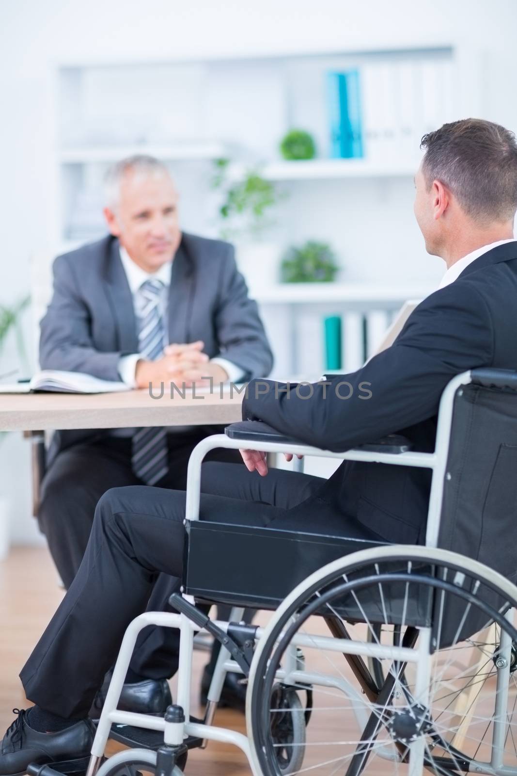 Businessman in wheelchair speaking with colleague in the office