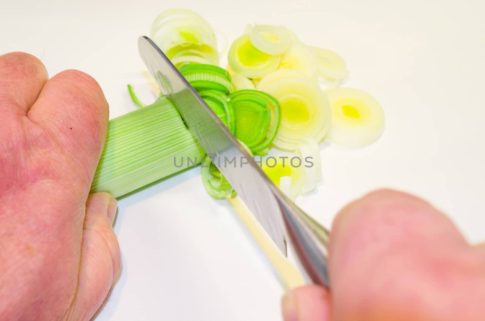 Hand of the cook, while cutting vegetables on a wooden board.