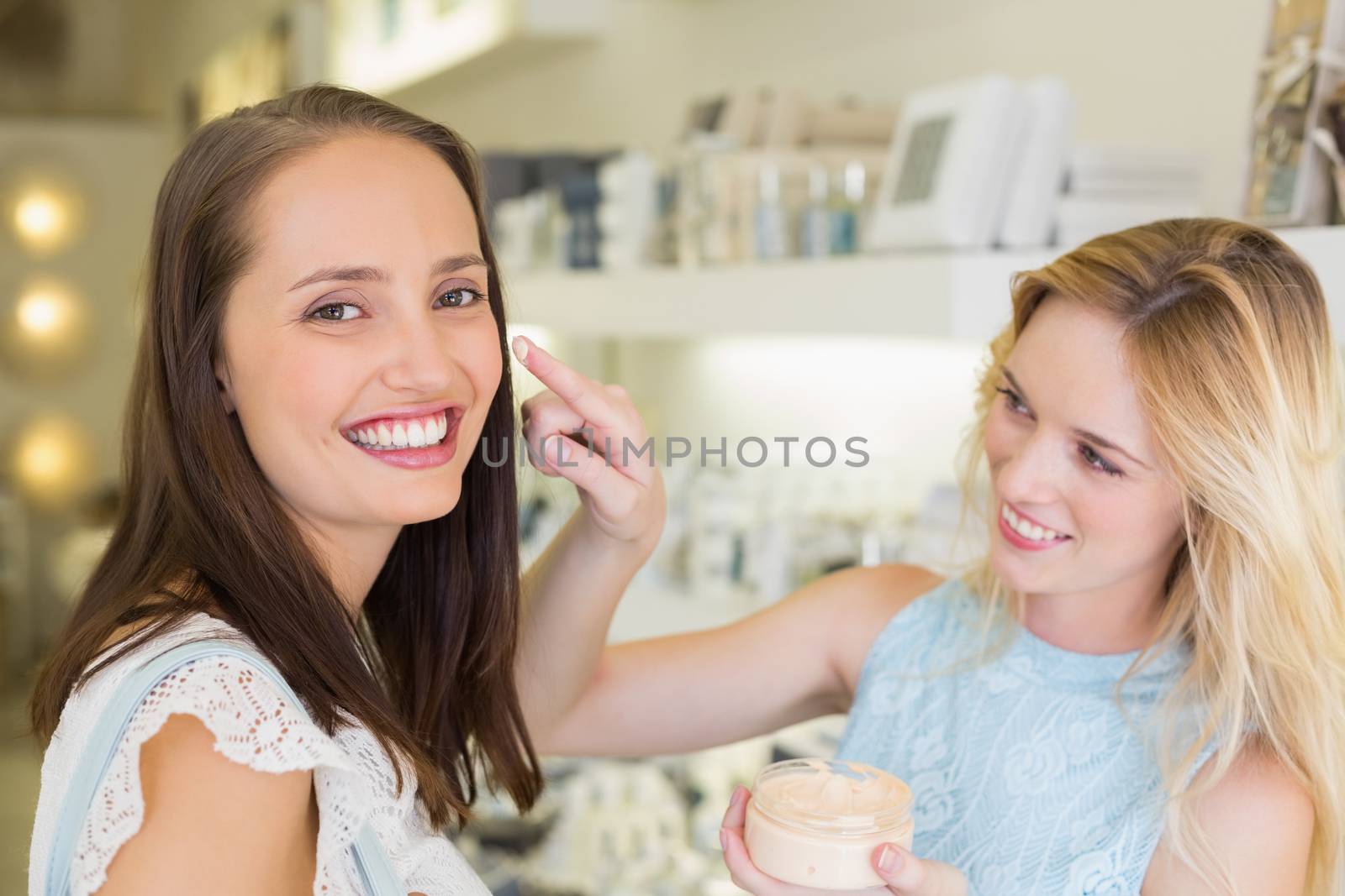 Happy blonde woman applying cosmetic products on her friend in a beauty salon