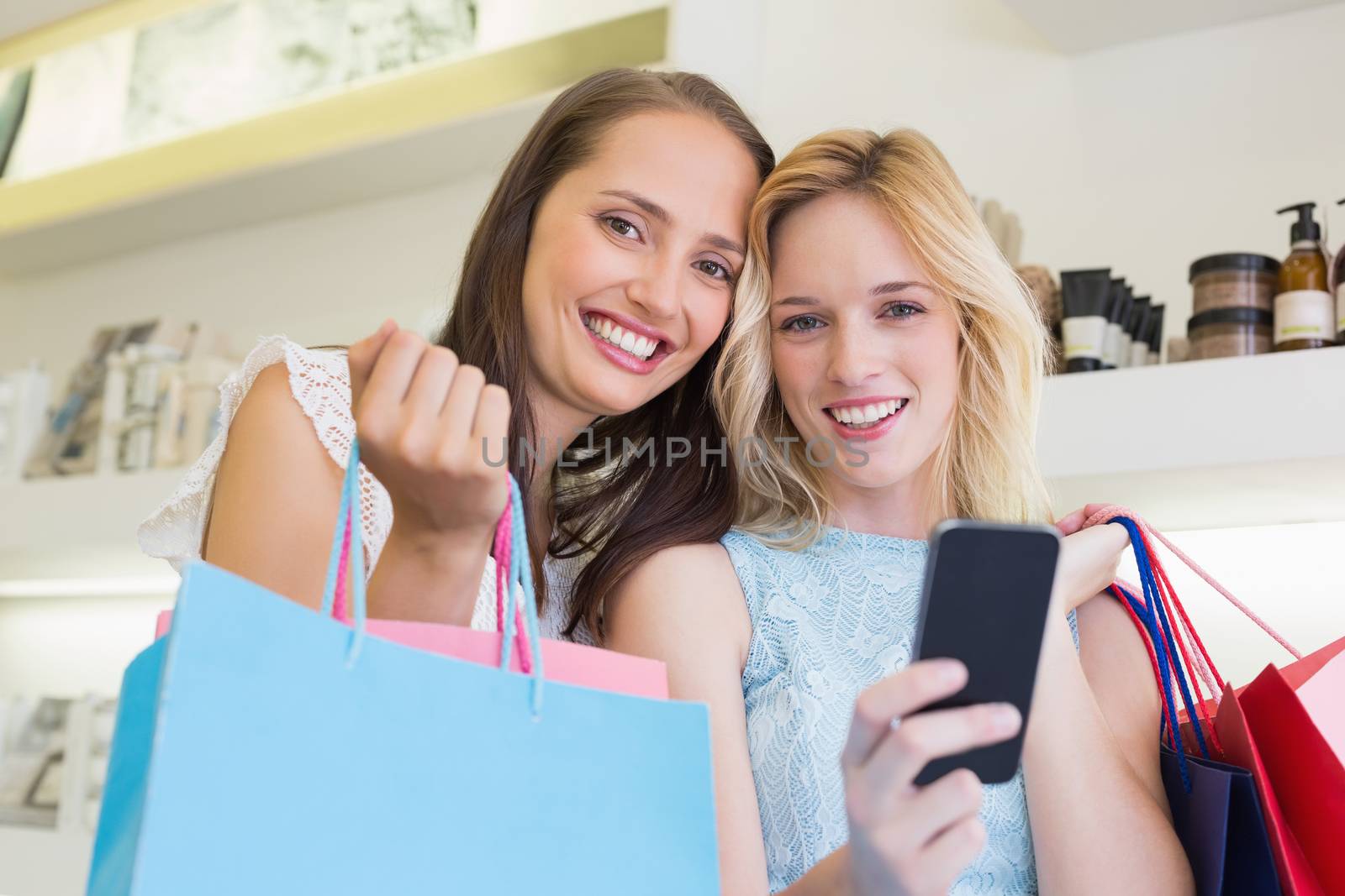 Happy women smiling at camera and holding smartphone in a beauty salon