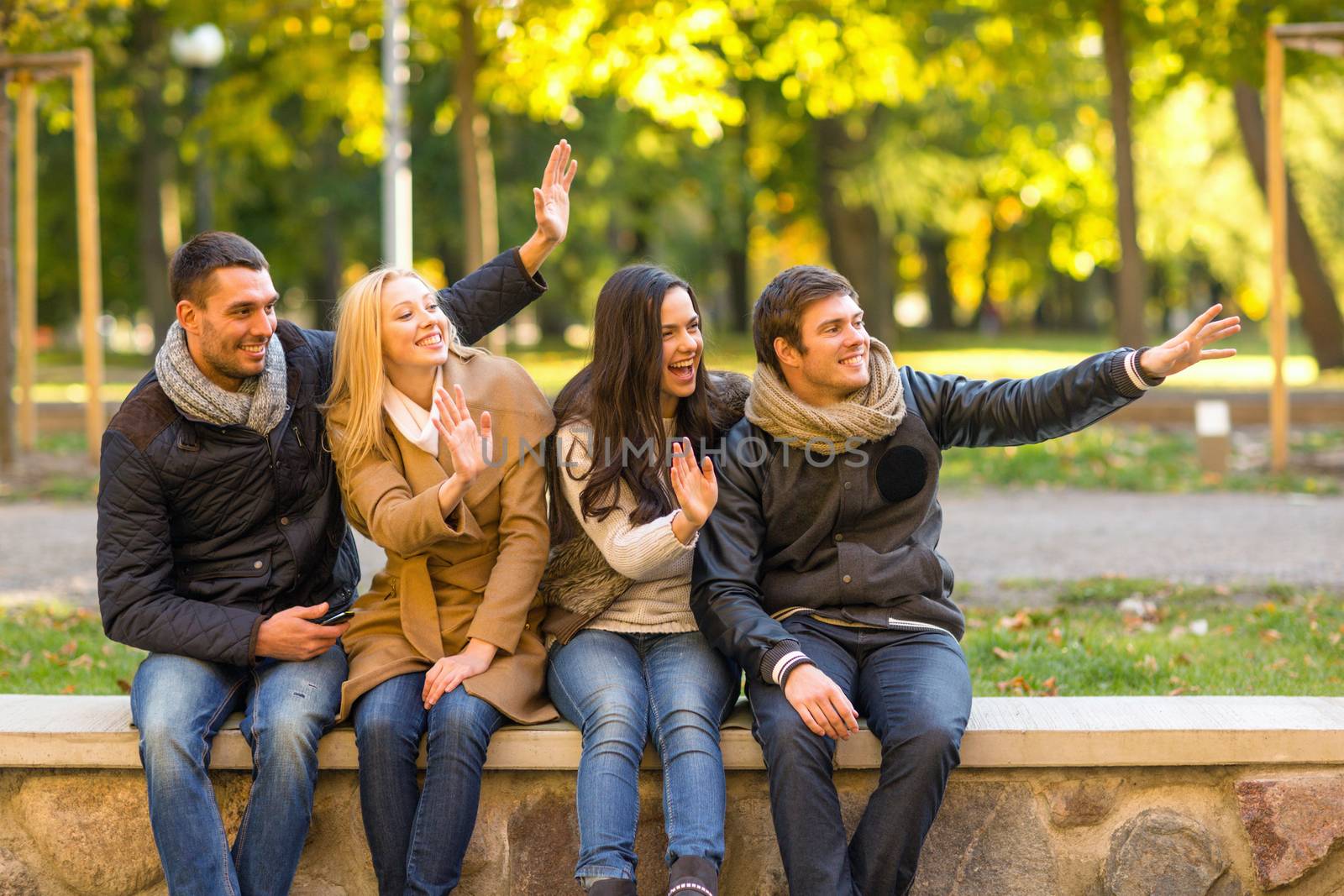 group of smiling friends waving hands in city park by dolgachov