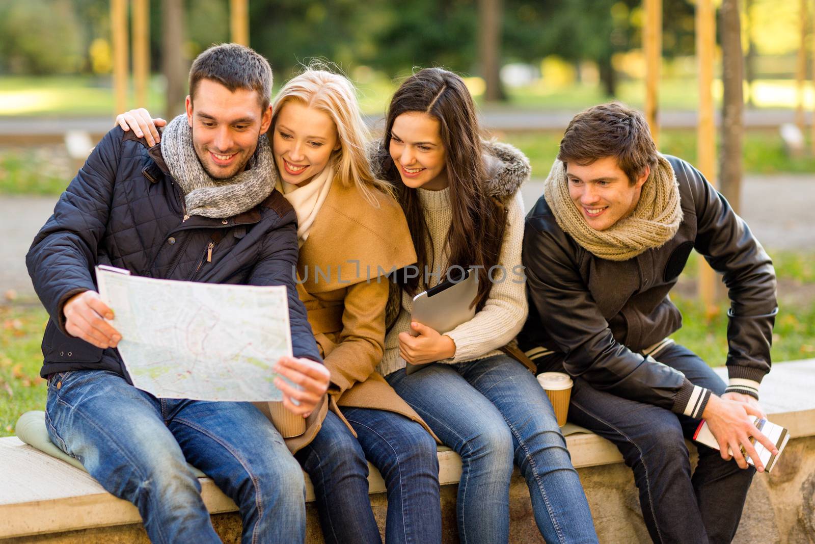 travel, vacation, people, tourism and friendship concept - group of smiling friends sitting with tablet pc computer city guide and map in park