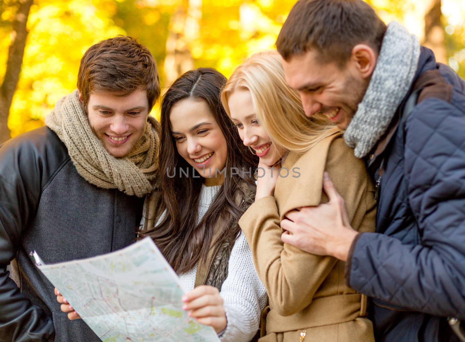 travel, vacation, people, tourism and friendship concept - group of smiling friends looking to map in city park