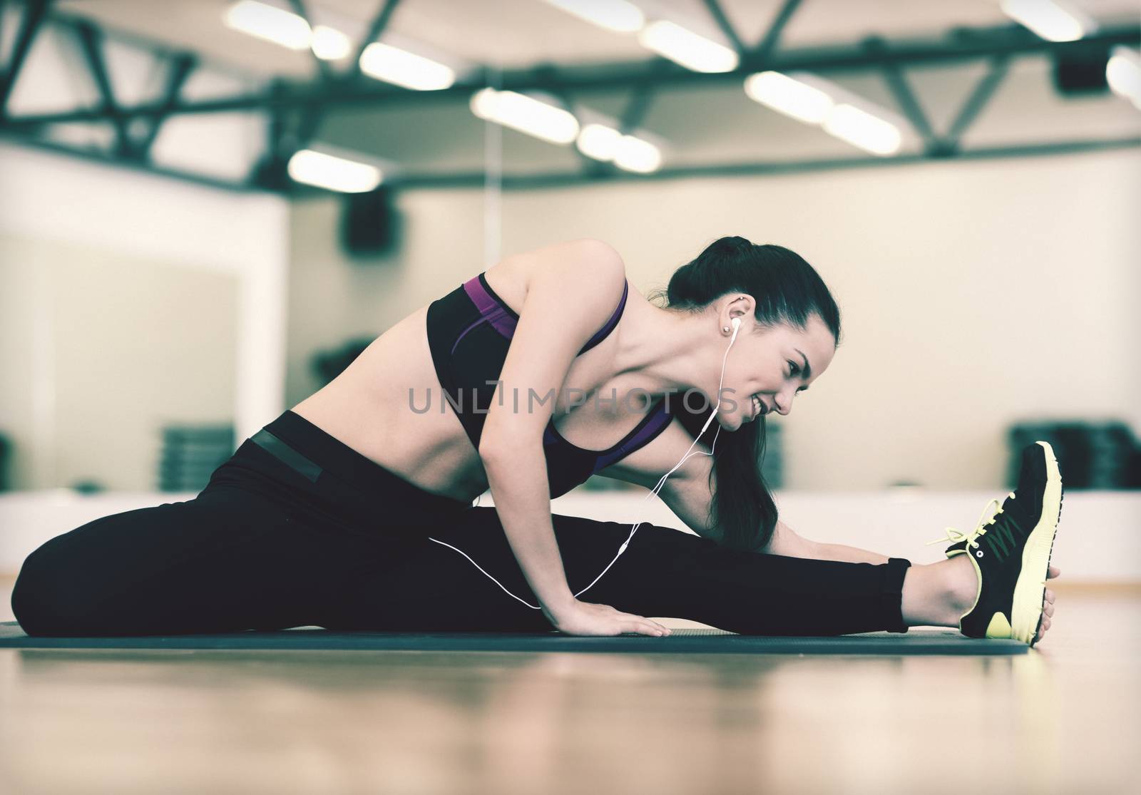 fitness, sport, training, gym and lifestyle concept - smiling woman stretching on mat in the gym