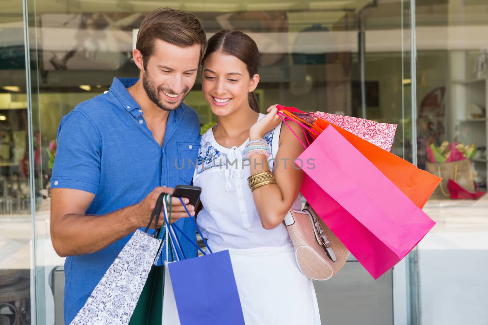Young happy couple looking at mobile phone after shopping