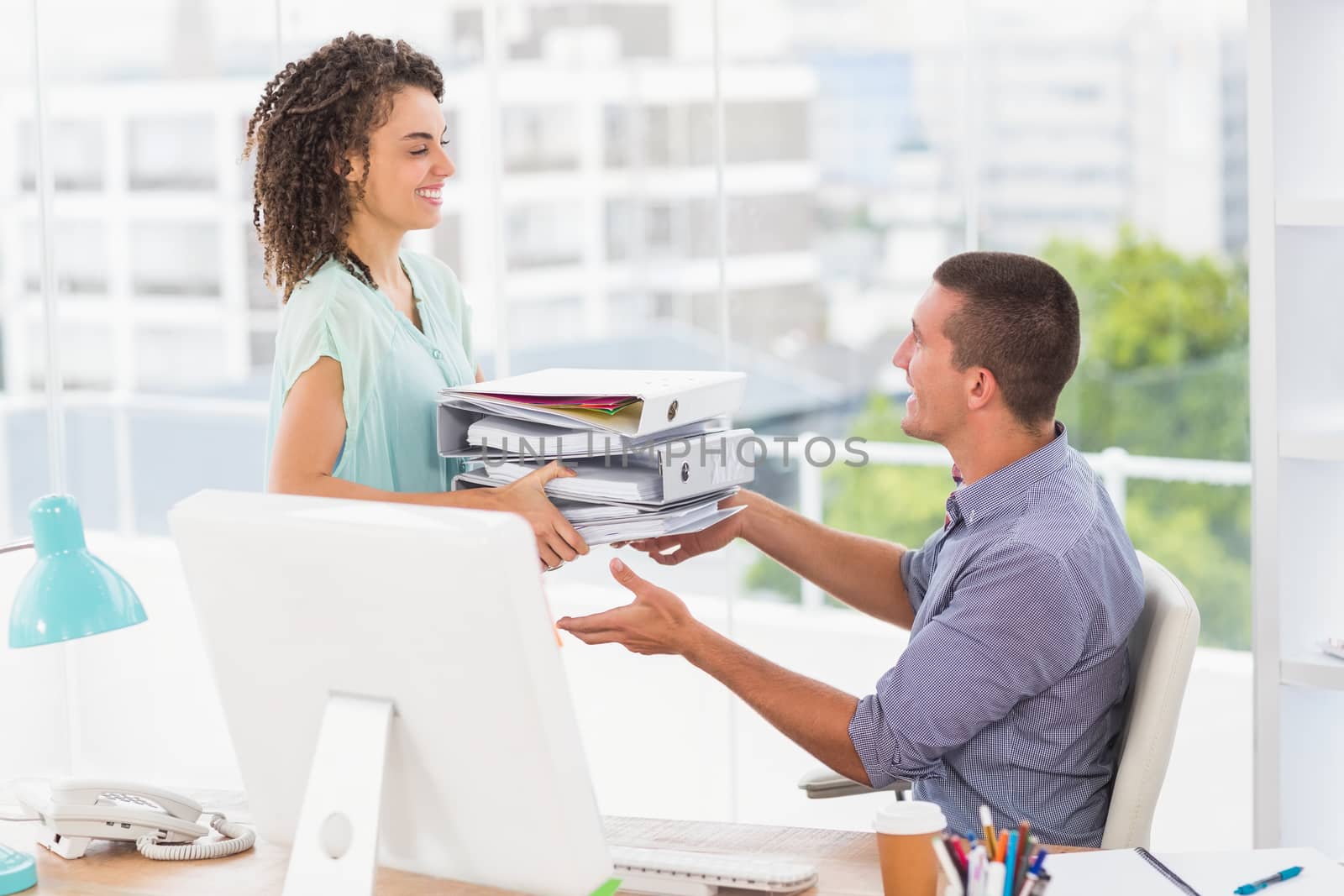 Businesswoman giving a stack of folders to her colleague by Wavebreakmedia