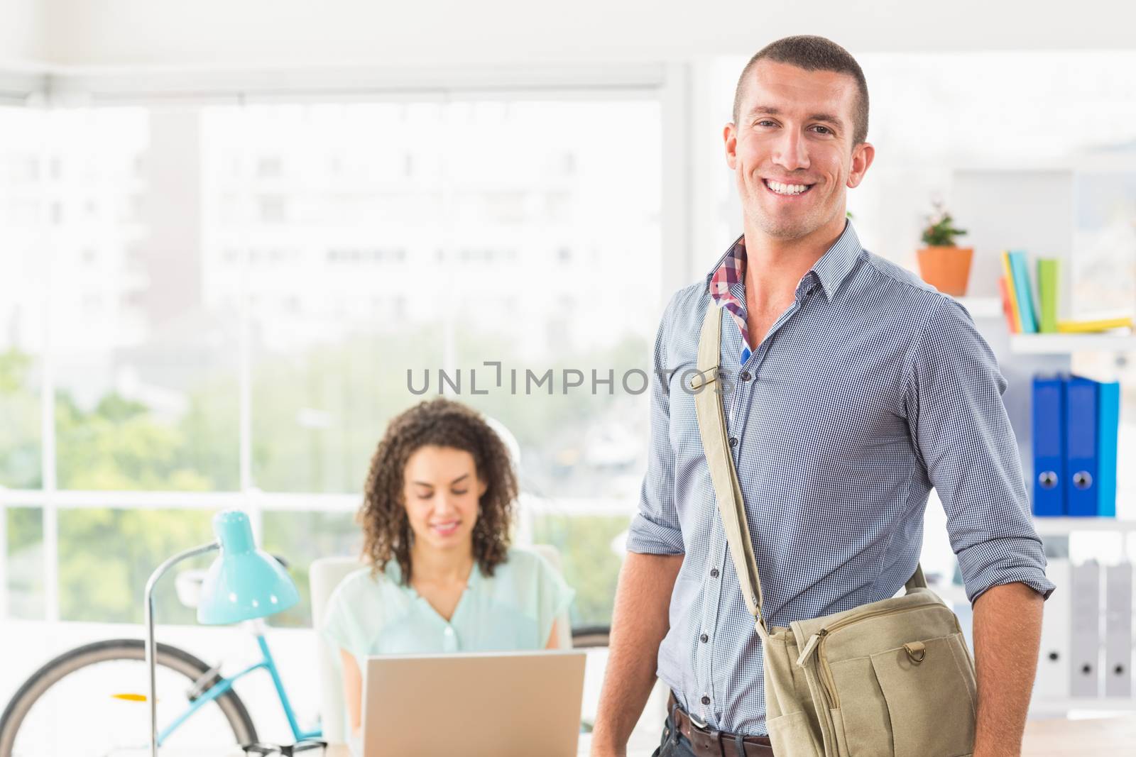 Creative businessman looking at the camera while his colleague working behind