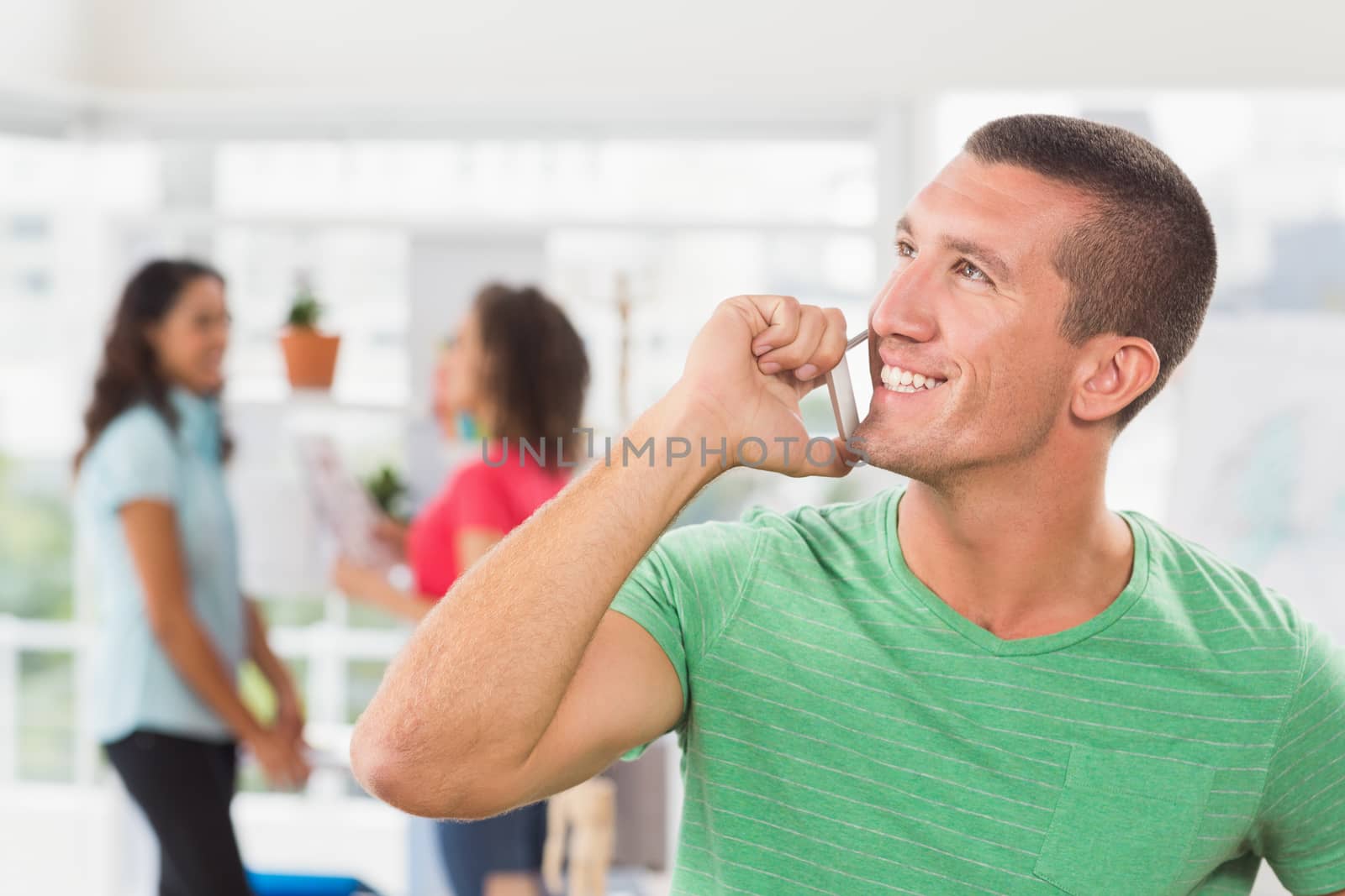 Businessman using his phone with two colleague behind him at the office