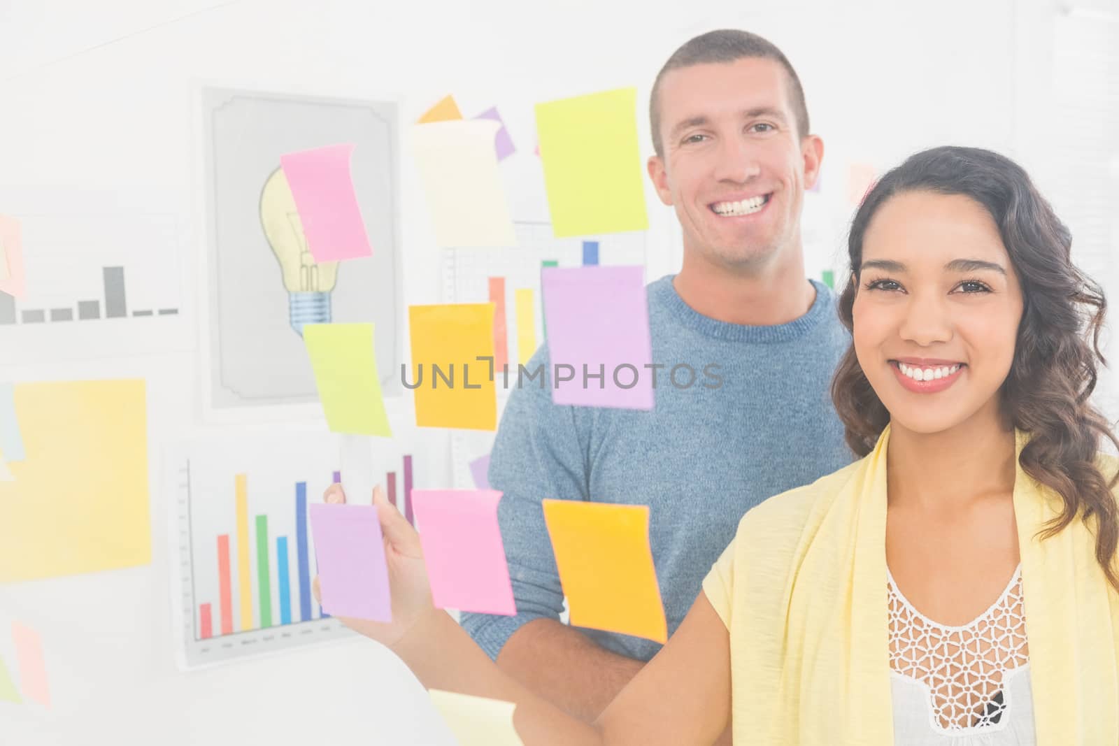 Portrait of smiling coworkers pointing sticky notes and looking at camera in the office