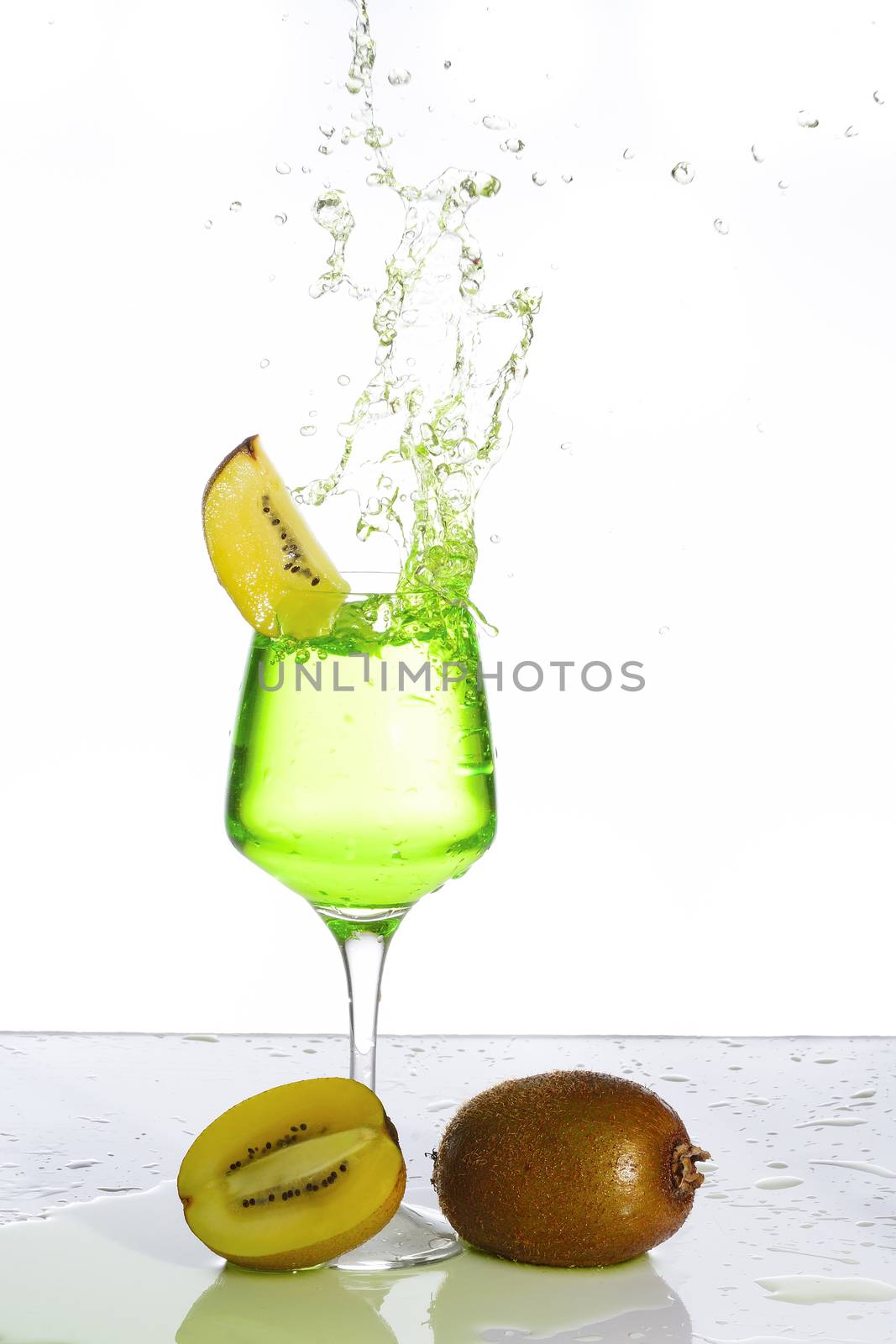 Stemmed champagne glass with kiwi liquor splashing out, isolated on white background