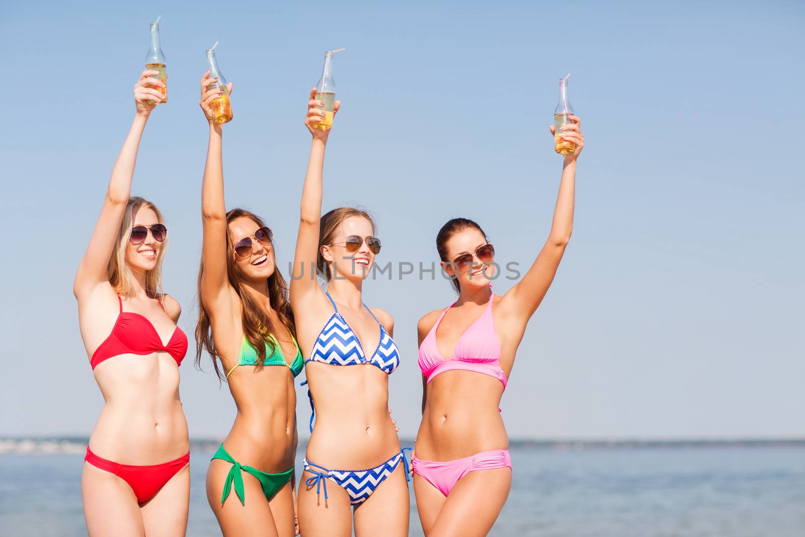 group of smiling young women drinking on beach by dolgachov