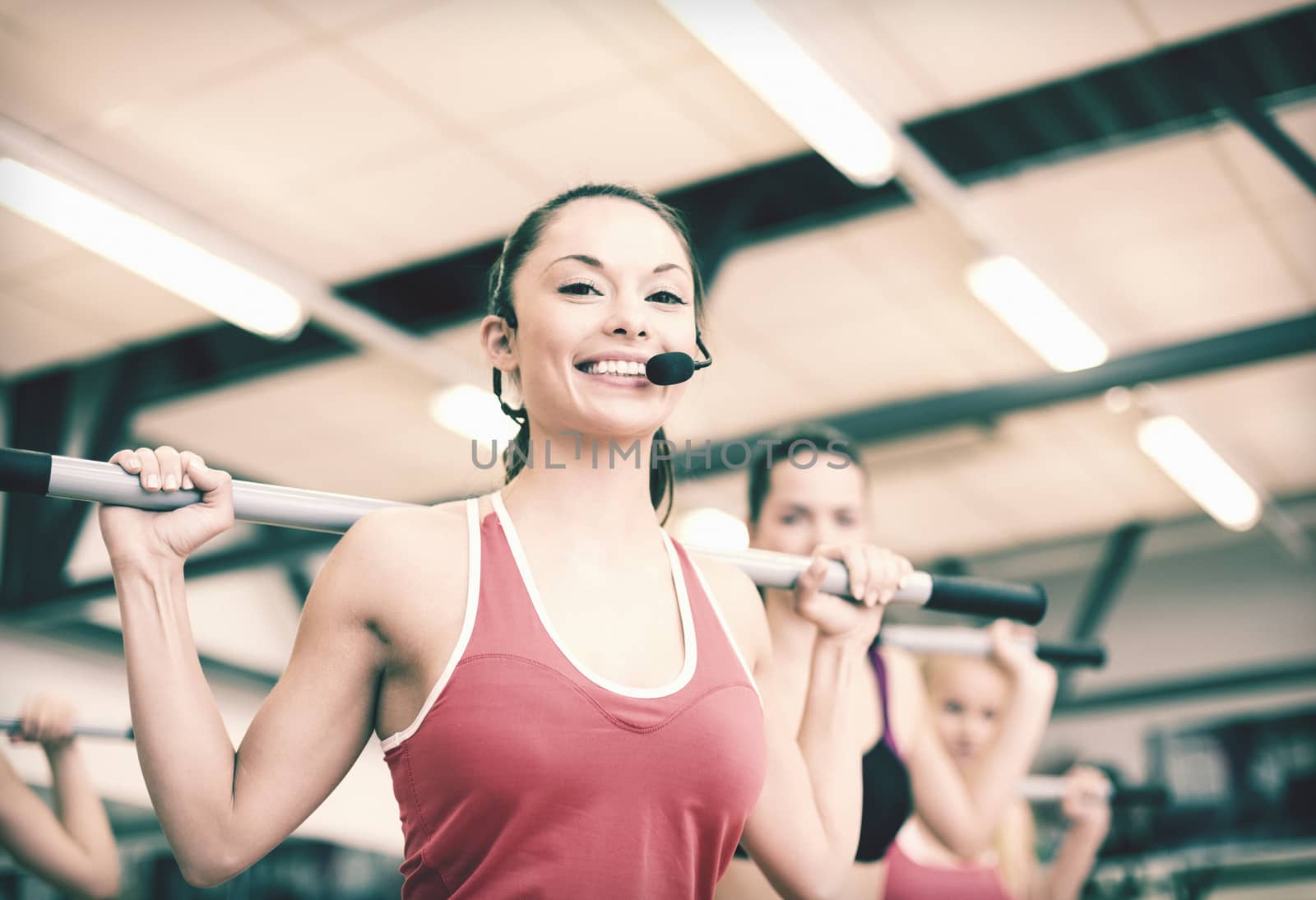 fitness, sport, training, gym and lifestyle concept - smiling trainer in front of the group of people working out with barbells in the gym