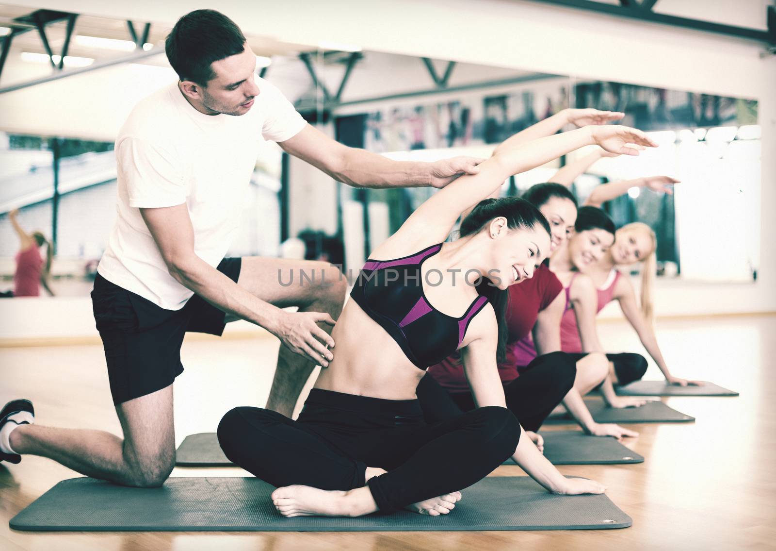 fitness, sport, training, gym and lifestyle concept - group of smiling women with male trainer stretching on mats in the gym