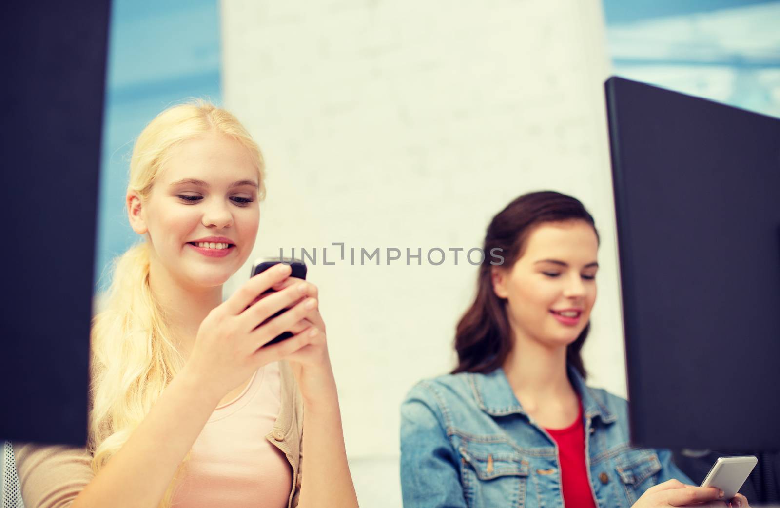 school, education, technology and internet concept - two teens with smartphones in computer class at school