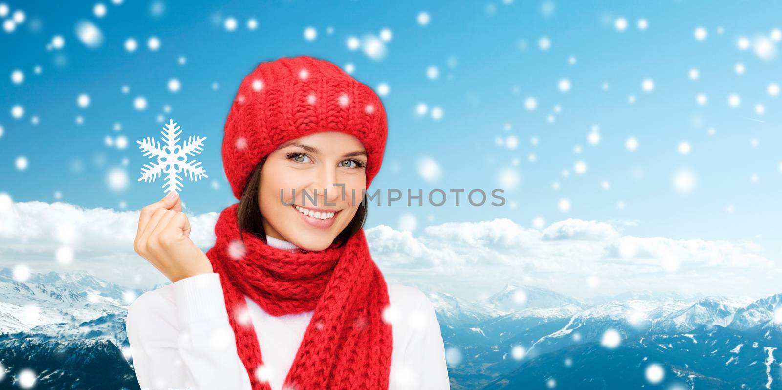 happiness, winter holidays, tourism, travel and people concept - smiling young woman in red hat and mittens holding snowflake over snowy mountains background