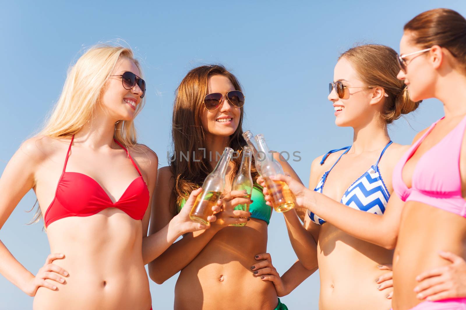 summer vacation, holidays, travel and people concept - group of smiling young women sunbathing and drinking on beach