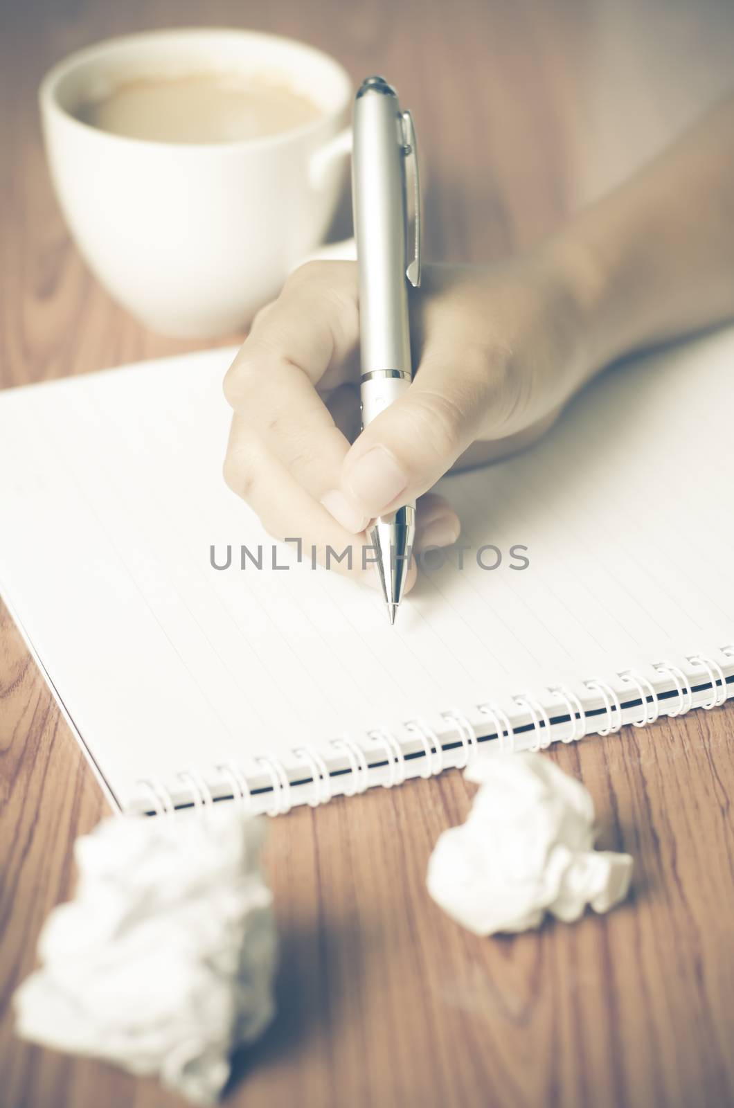 woman hand writing with pen on notebook.there are crumpled paper and coffee cup on wood table background vintage style