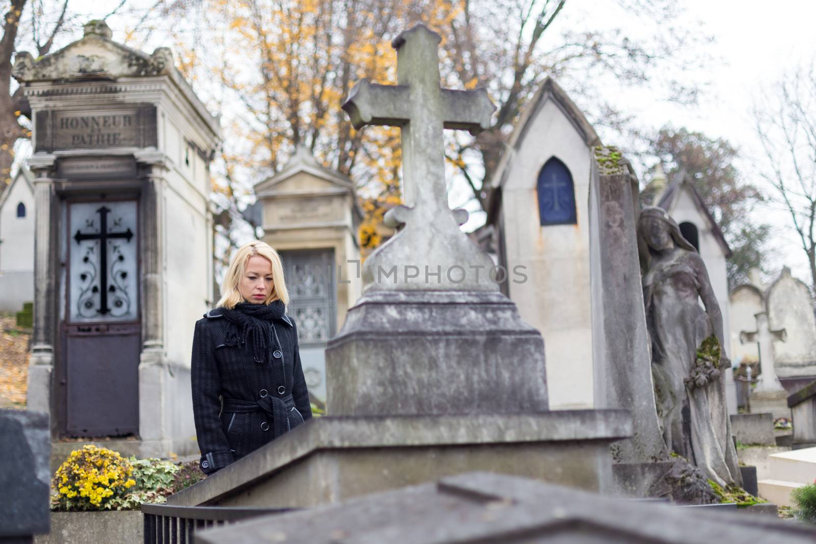 Solitary woman mourning by gravestone, remembering dead relatives in on Pere Lachaise cemetery in Paris, France.