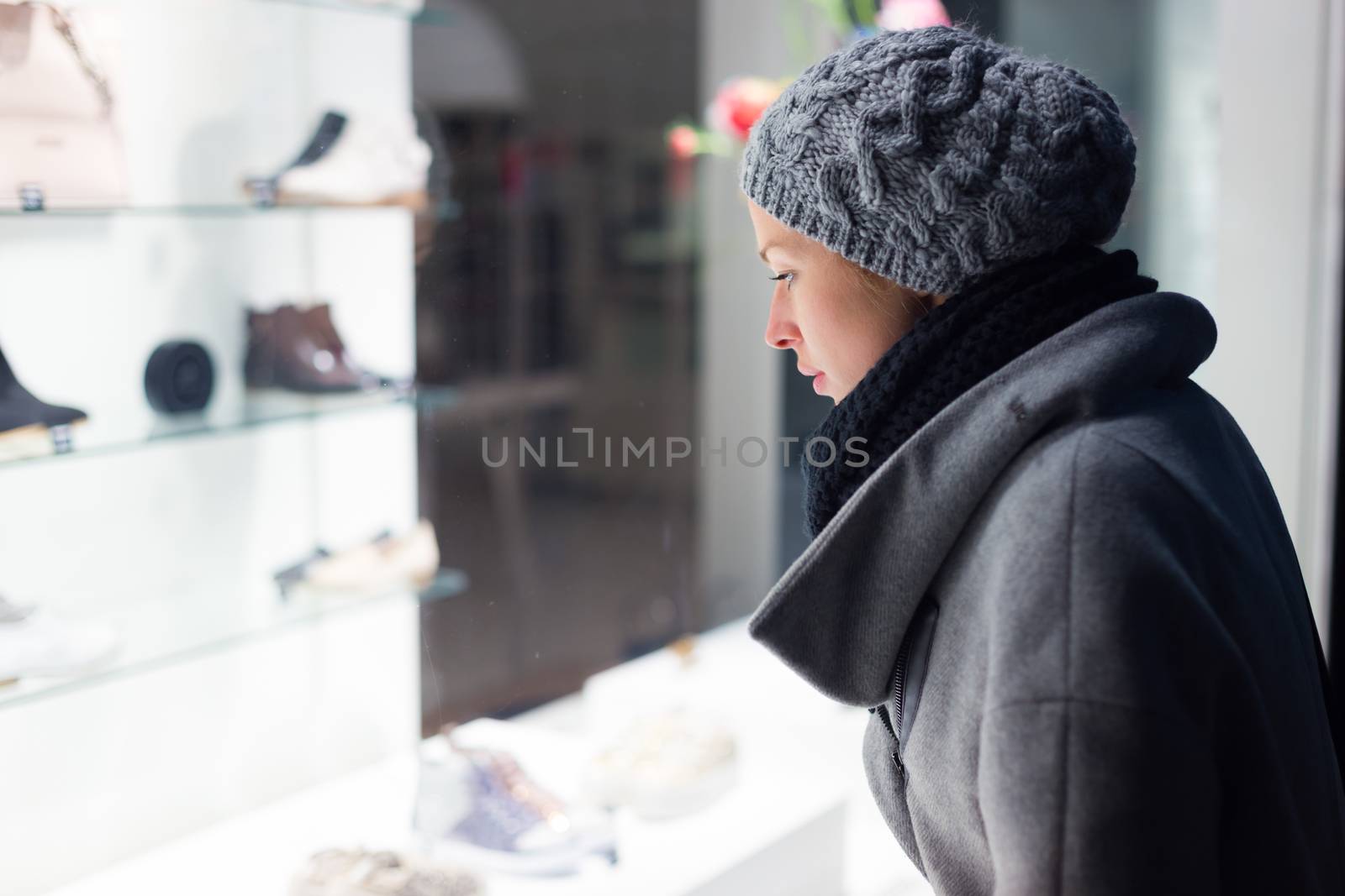 Casualy winter dressed lady window shopping in front of sinfully expensive boutique store dispaly window. Customer woman in shopping street, looking at window, outdoor.