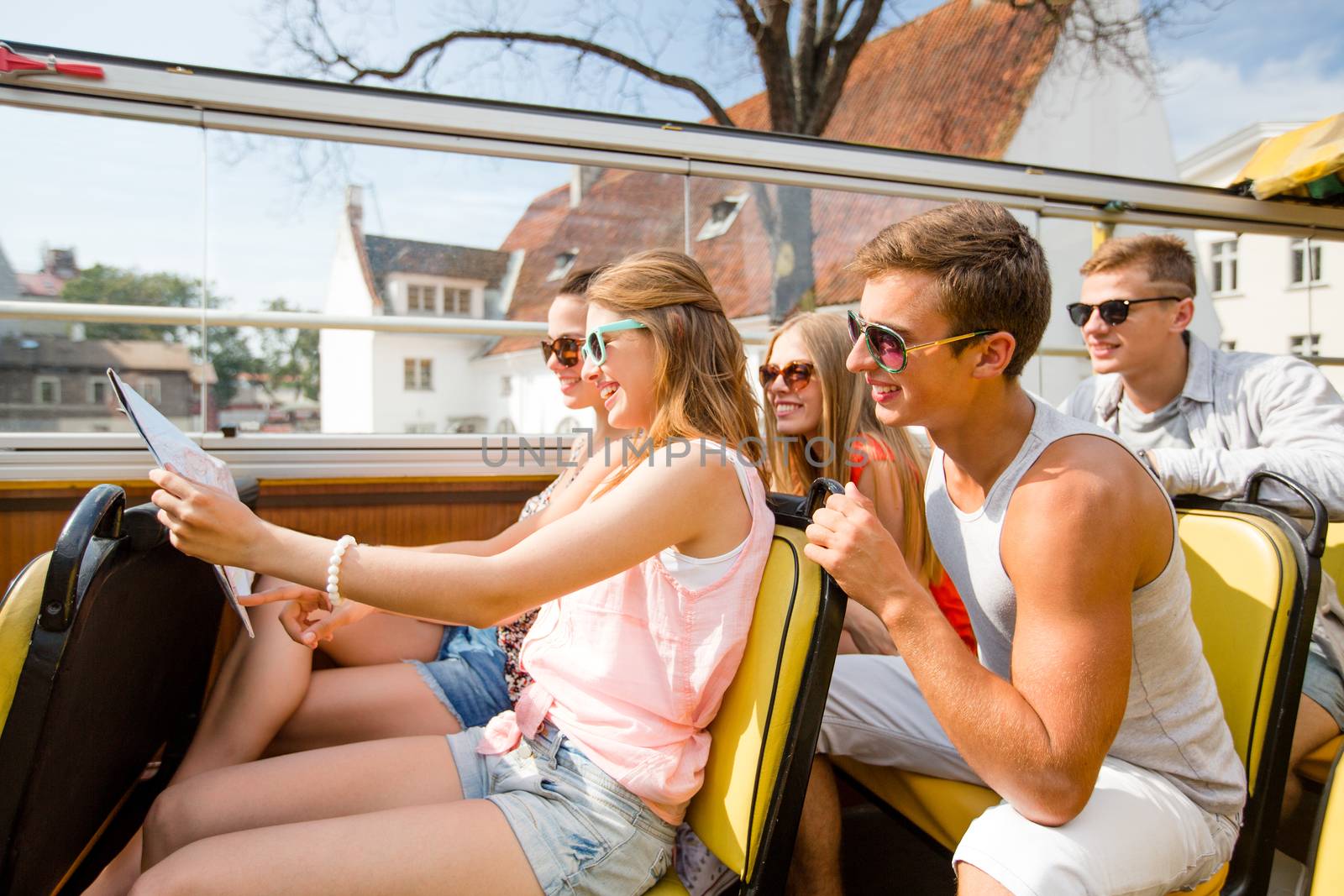 friendship, travel, vacation, summer and people concept - group of smiling friends with map traveling by tour bus