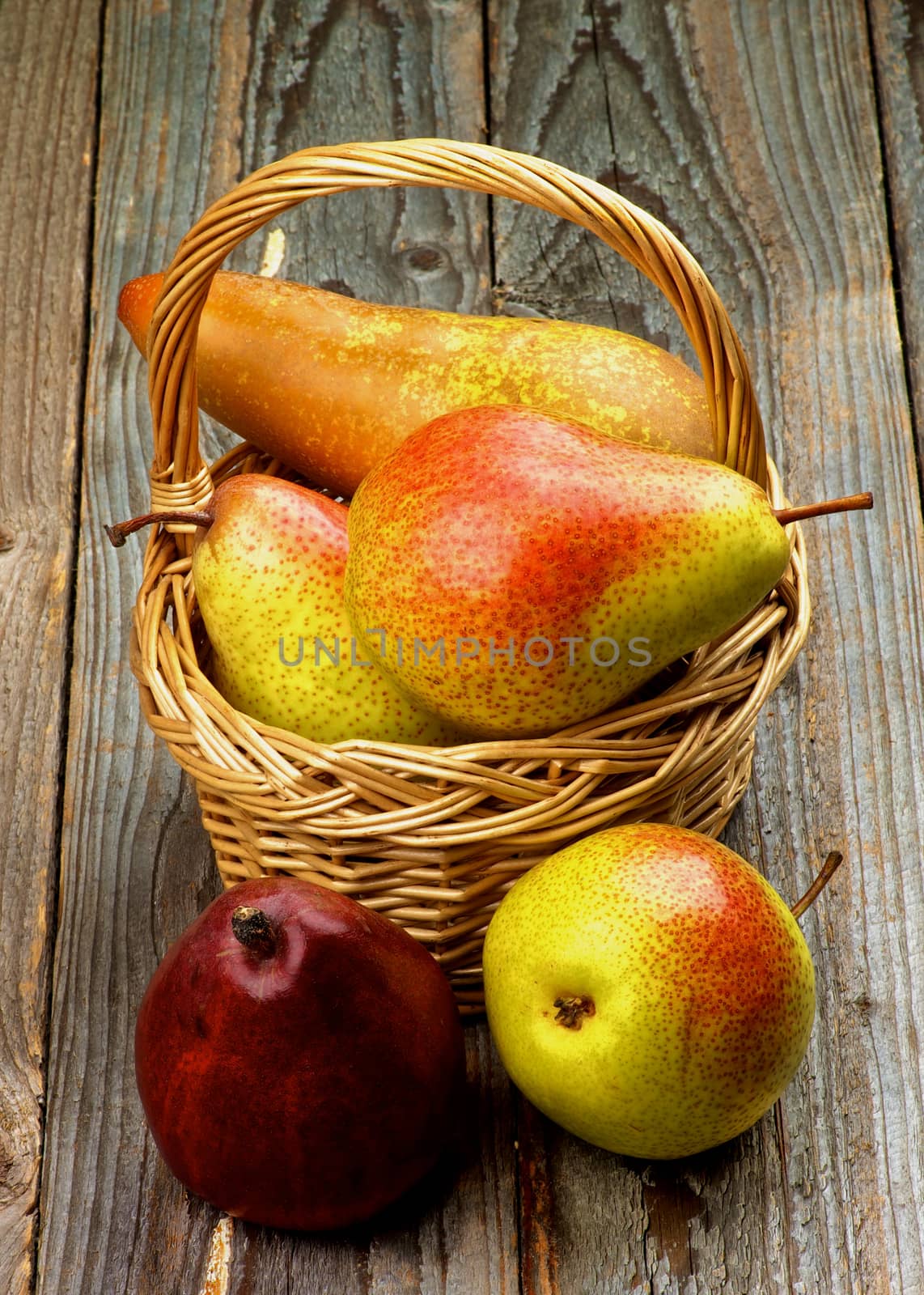 Arrangement of Yellow, Red and Conference Pears in Wicker Basket closeup on Rustic Wooden background