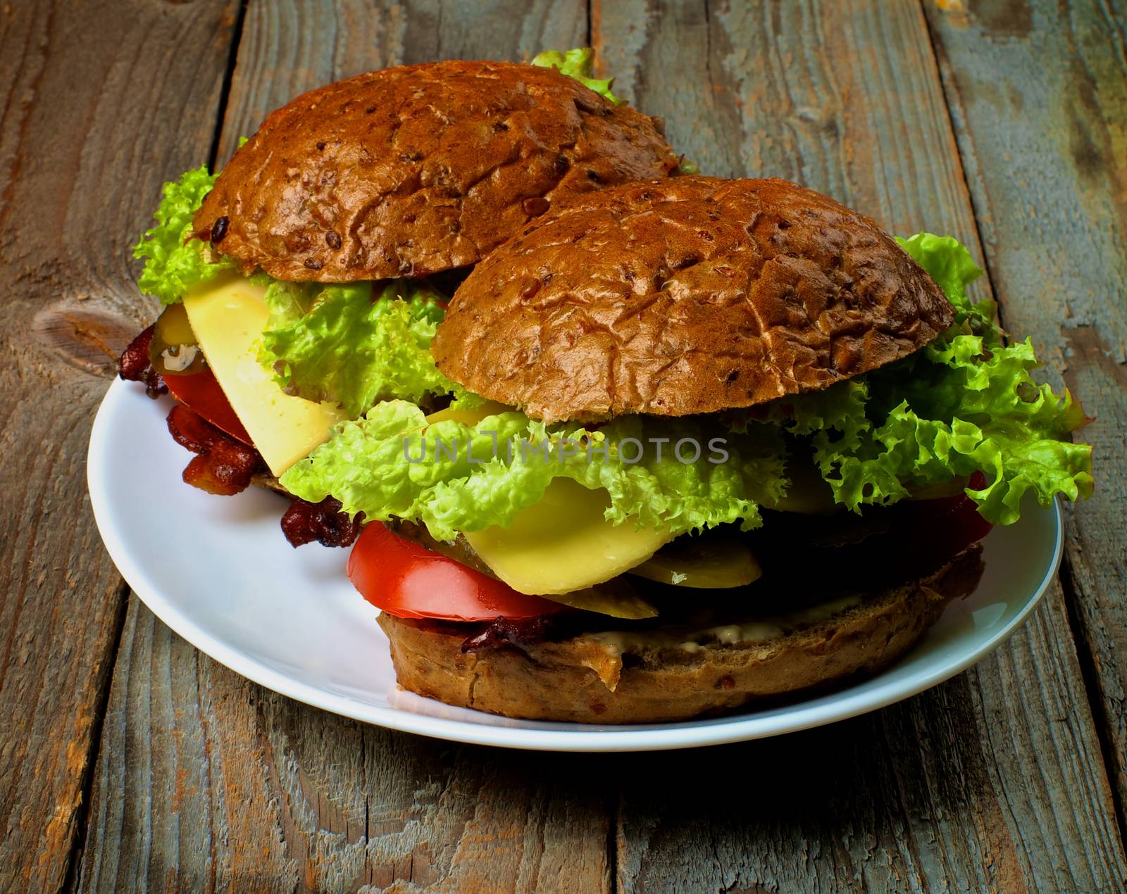 Homemade Hamburgers with Bacon Lettuce,Tomato, Onions, Cheese, and Pickled Cucumber with Whole Wheat Bun on White Plate closeup on Rustic Wooden background