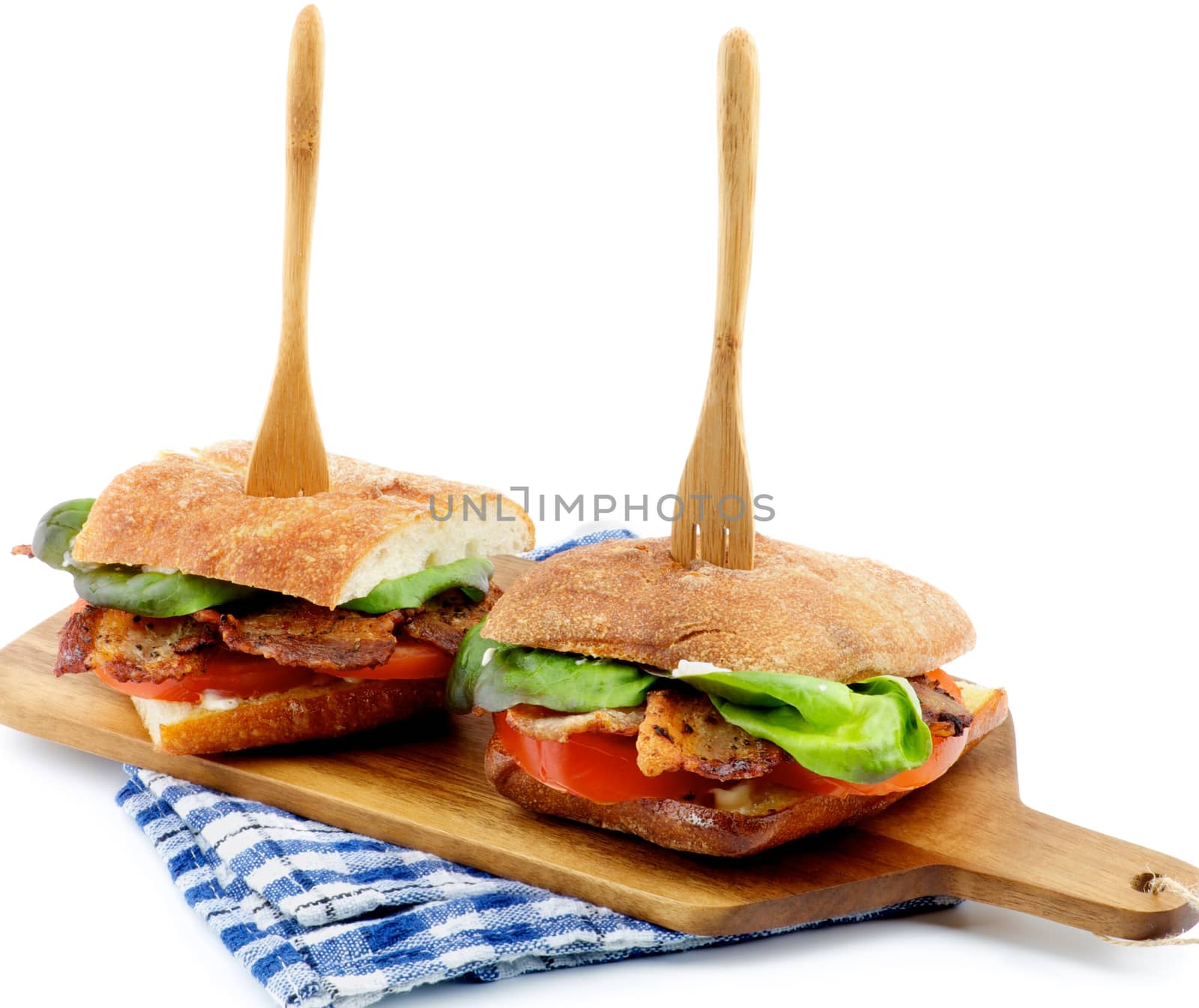 Ciabatta Sandwiches with Bacon, Tomato, Lettuce and Sauces on Cutting Board Arranged with Wooden Fork closeup on white background