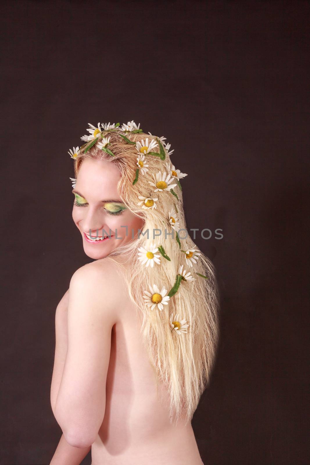 Half Body Shot of a Happy Bare Young Woman with Flowers on her Long Blond Hair, Looking on her Shoulder Against Black Background.
