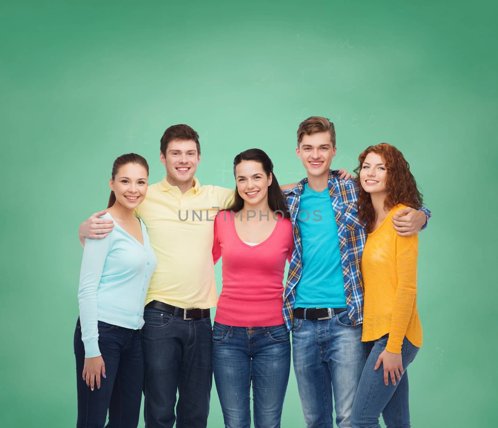 friendship, education, school and people concept - group of smiling teenagers standing and hugging over green board background