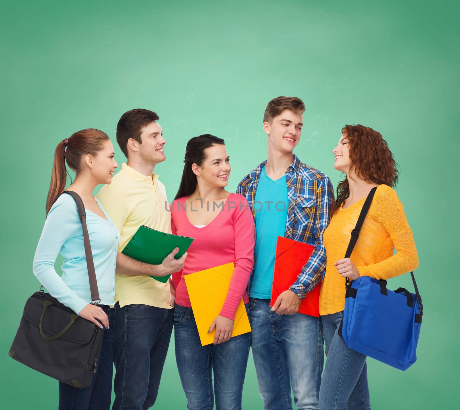 friendship, education and people concept - group of smiling teenagers with folders and school bags over green board background