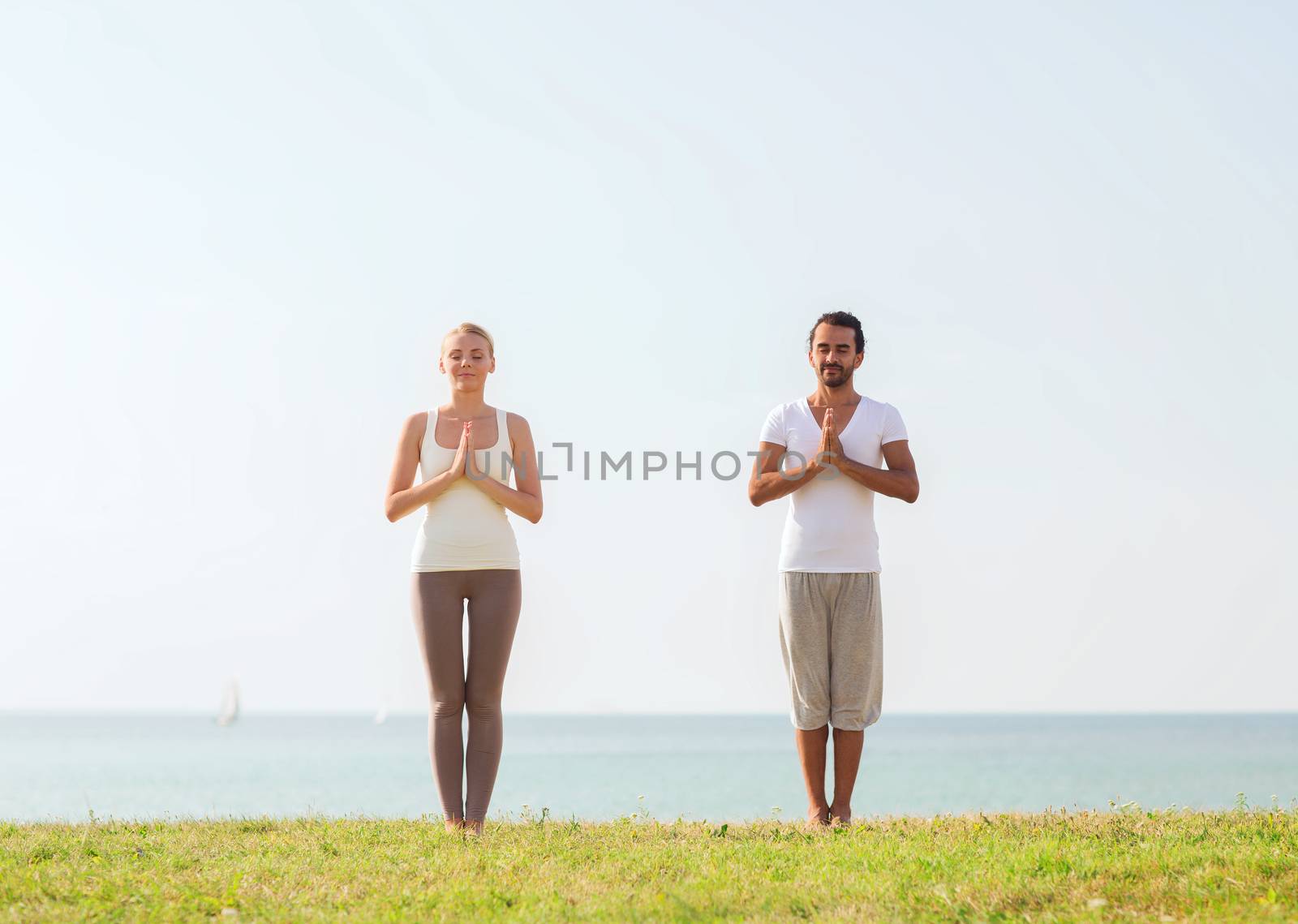 smiling couple making yoga exercises outdoors by dolgachov