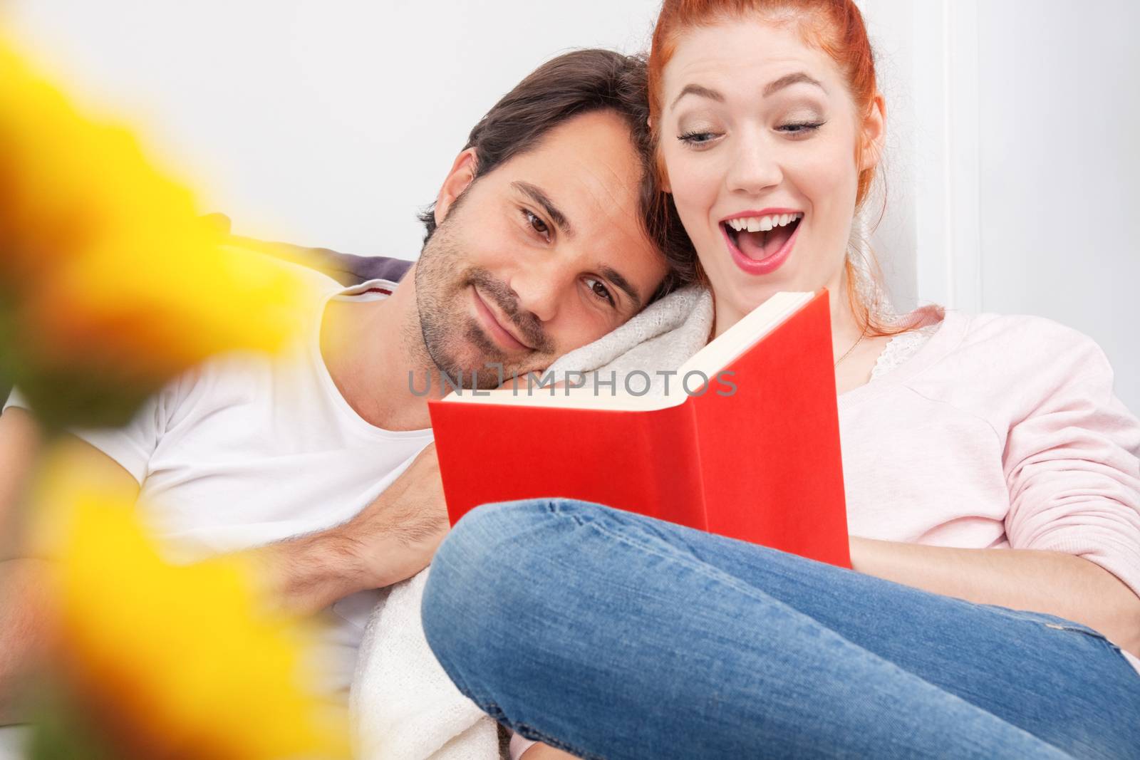 Close up Sweet Young Couple Sitting at the Couch In the Living Room, Reading a Book Together with Happy Facial Expressions.