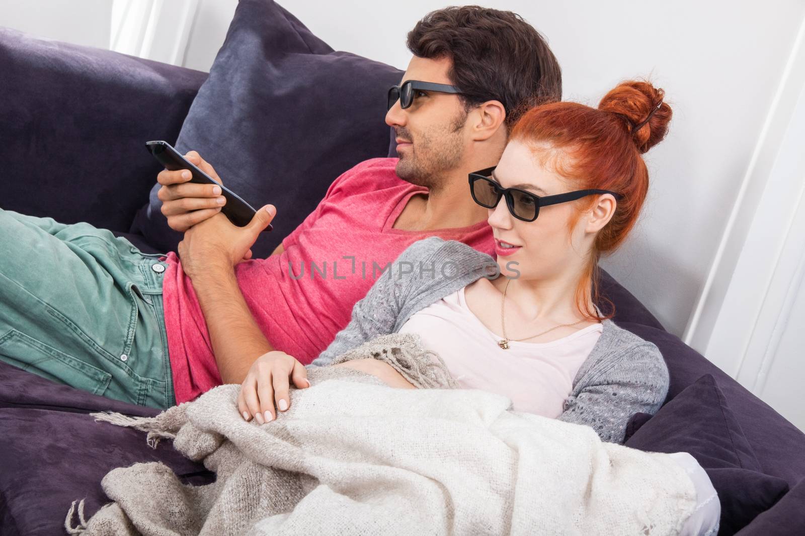 Young Couple Wearing 3D Glasses, Sitting on the Couch in the Living Room, Watching a Movie and Showing Shocked Faces.
