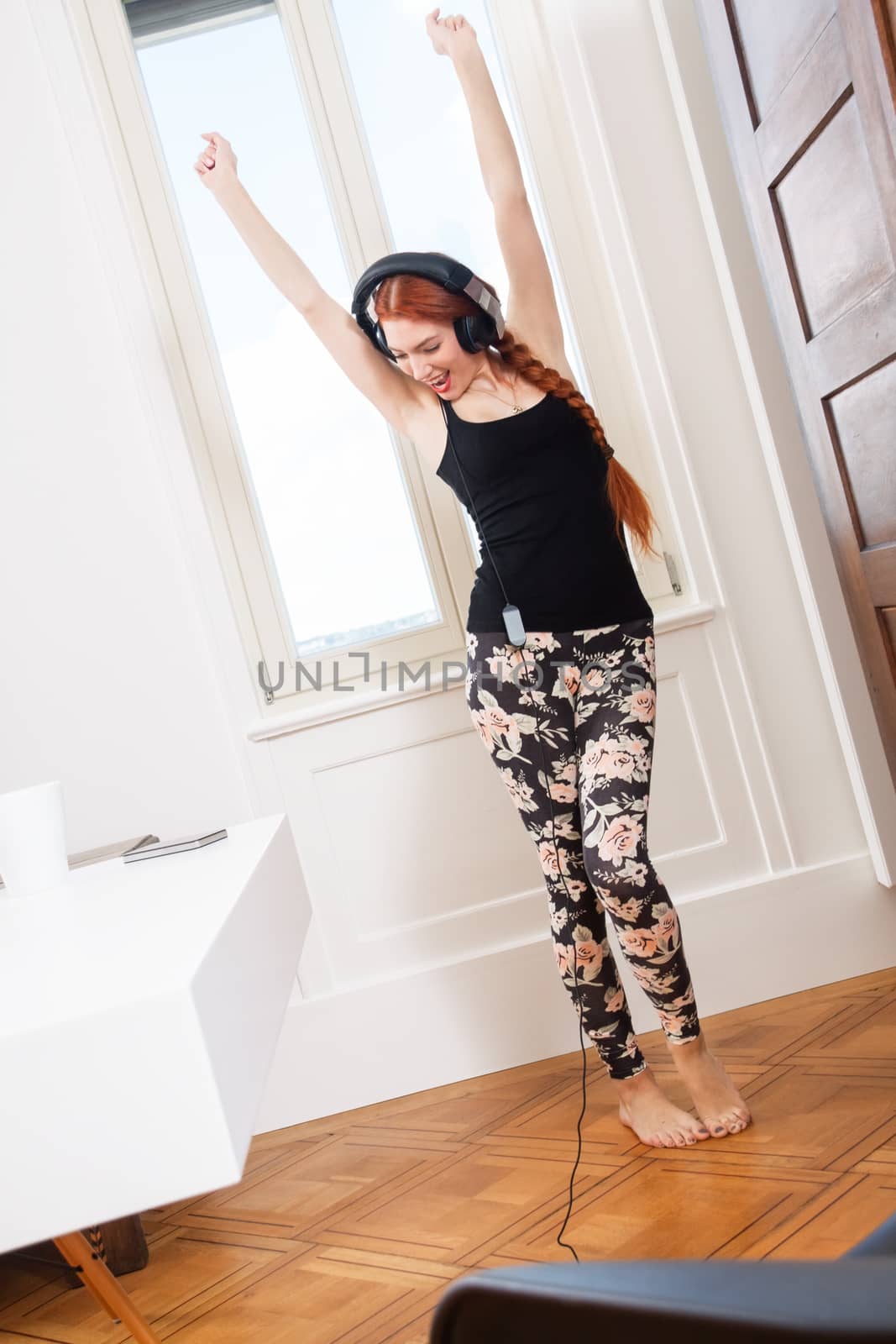 Happy Young Woman Dancing While Listening her Favorite Music Using Headphone Inside her Room.