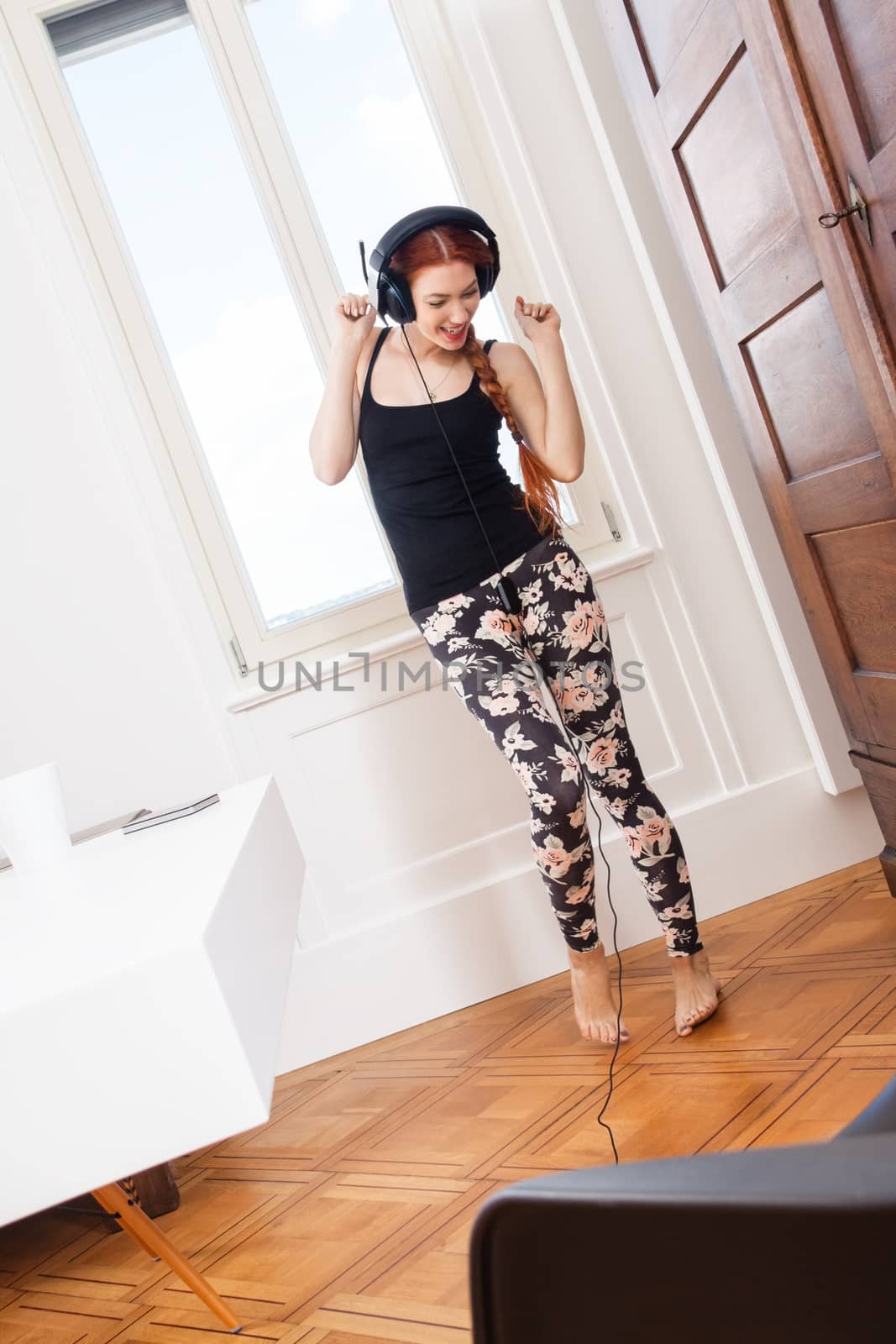 Happy Young Woman Dancing While Listening her Favorite Music Using Headphone Inside her Room.