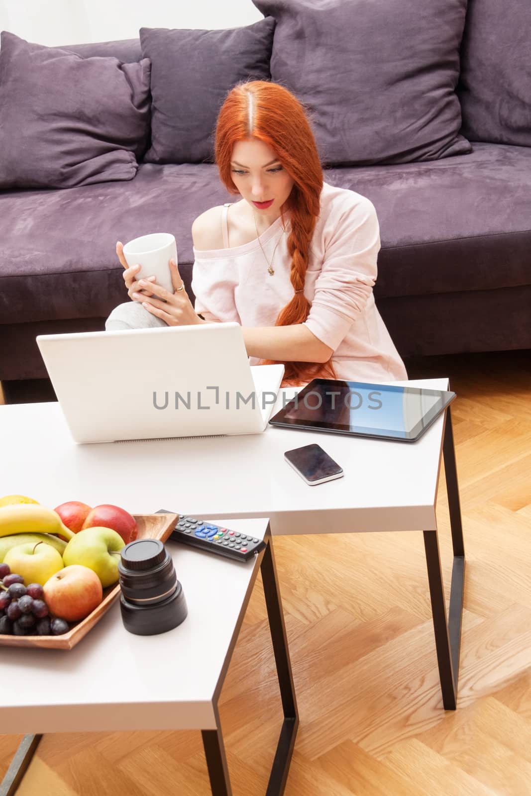 Pretty Young Woman Using her Laptop Computer In the Living Room with Feet on the Table and Showing Serious Face.